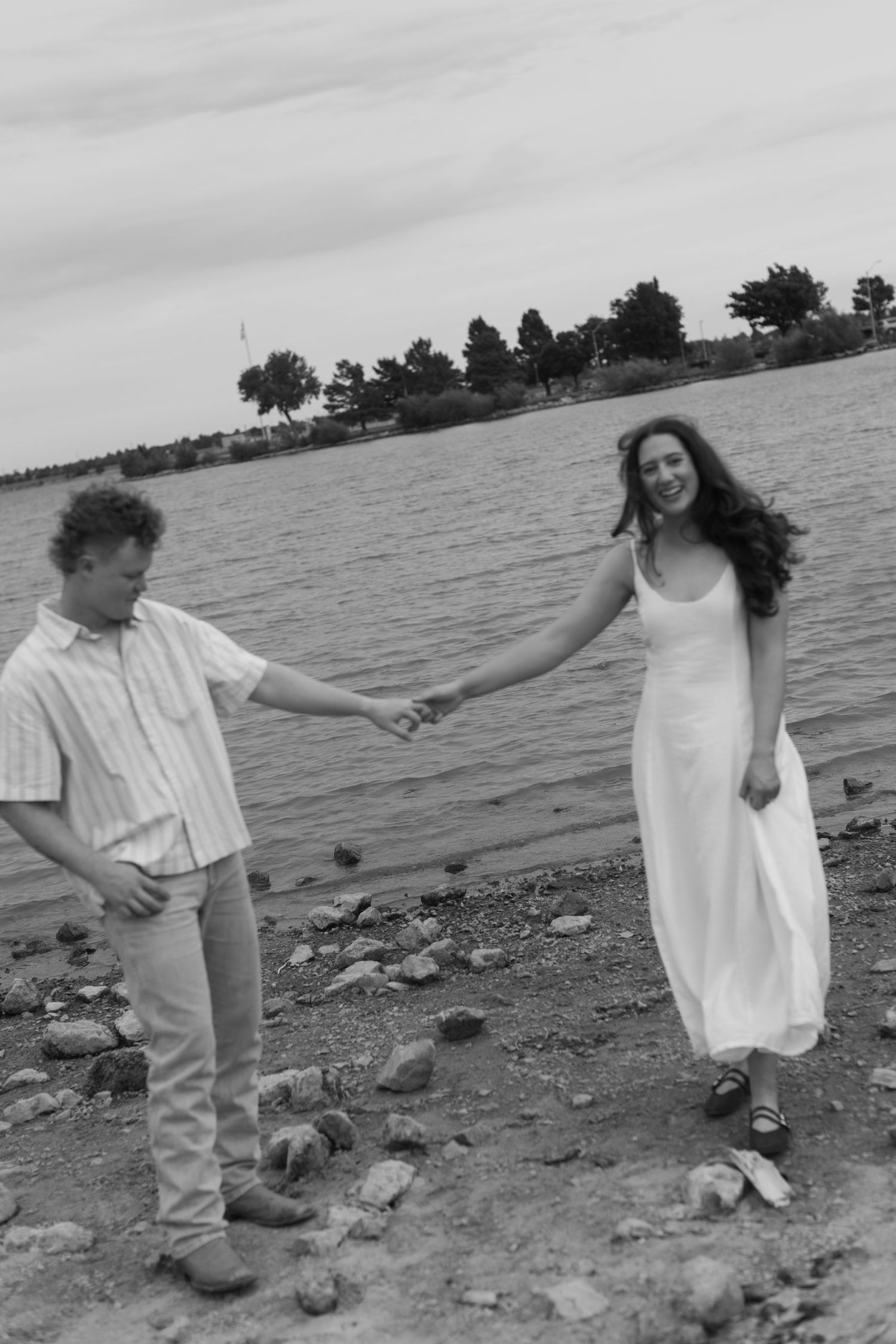 A couple dances and interacts romantically on a rocky shoreline in black and white tones.