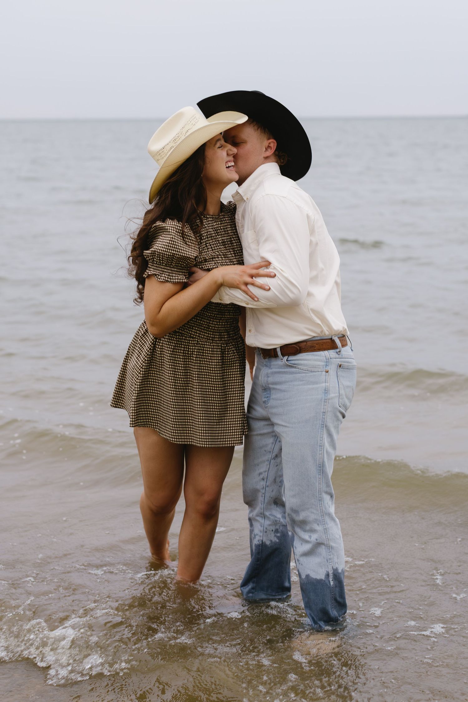 A couple splashes and plays together in shallow coastal waters during a beach photoshoot.