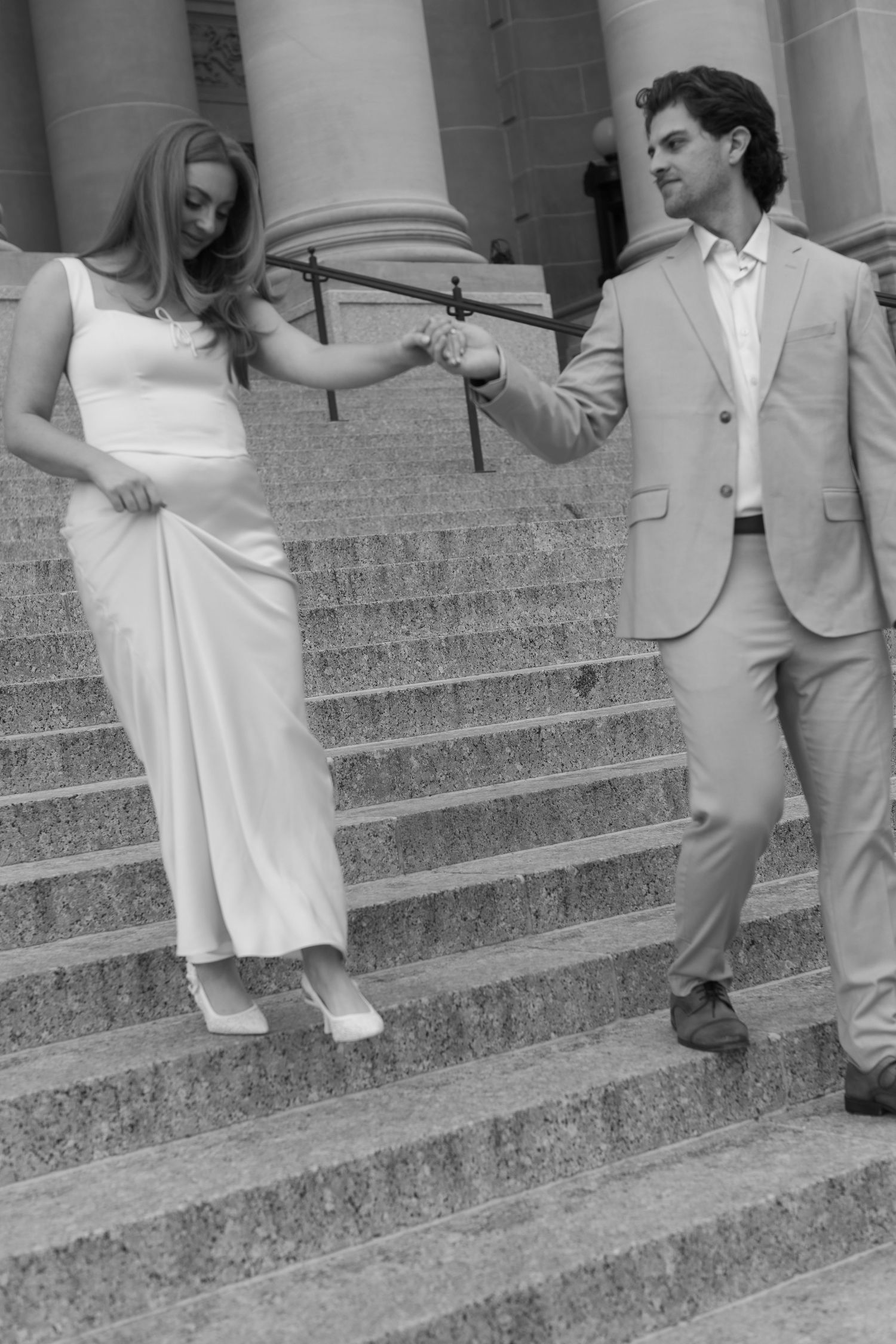 A couple shares playful moments on stone steps of a grand building.