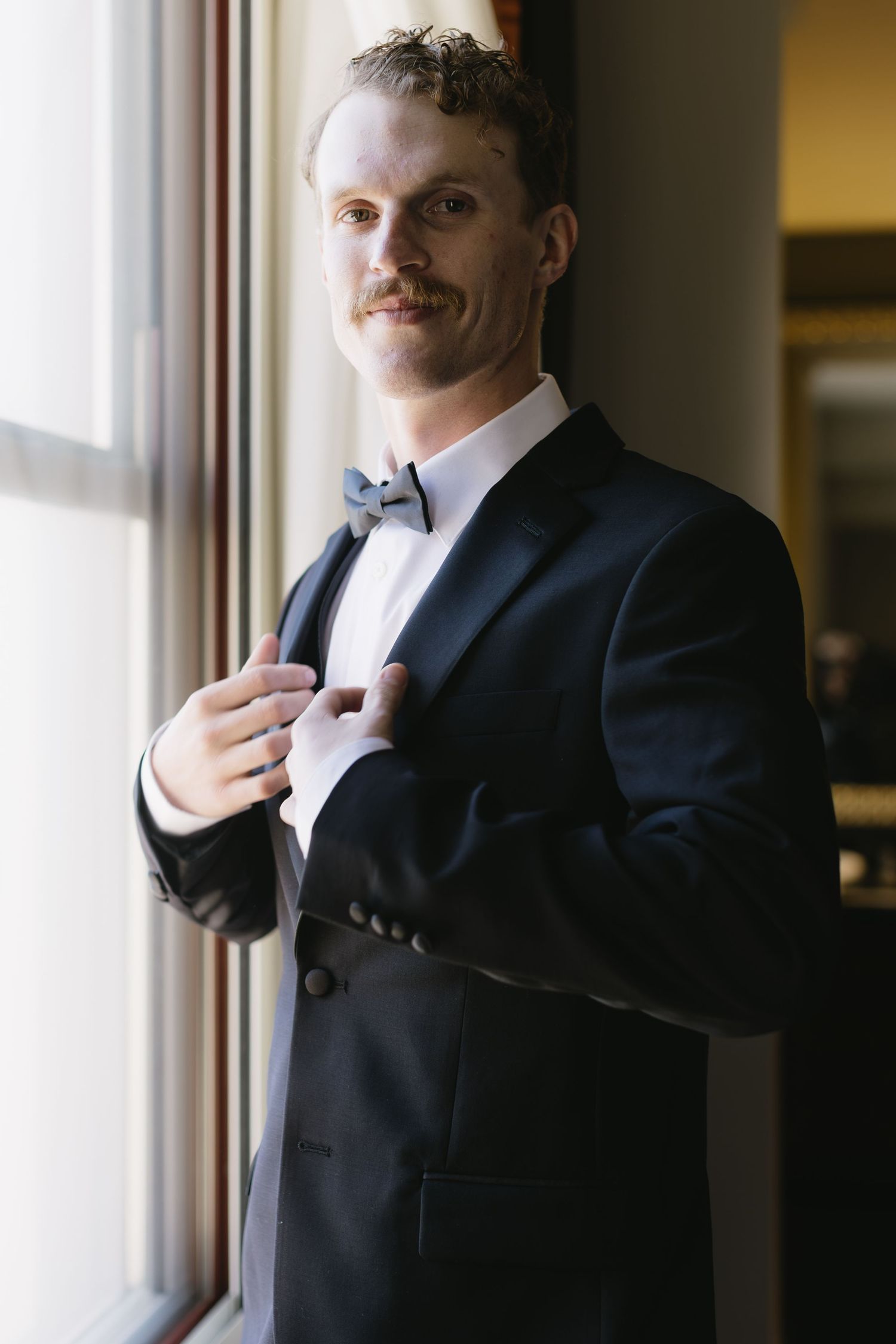 Close-up shots of formal black tuxedo and bowtie adjustments near window.