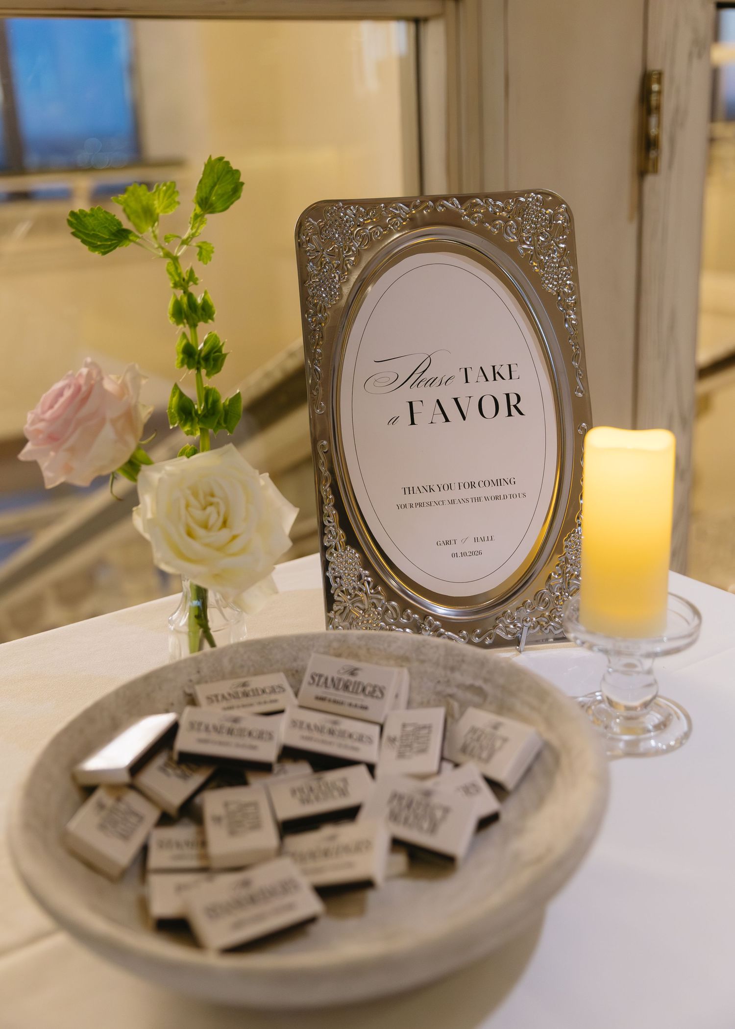 Wedding favor display with elegant frames, candles, and pink and white floral arrangements.