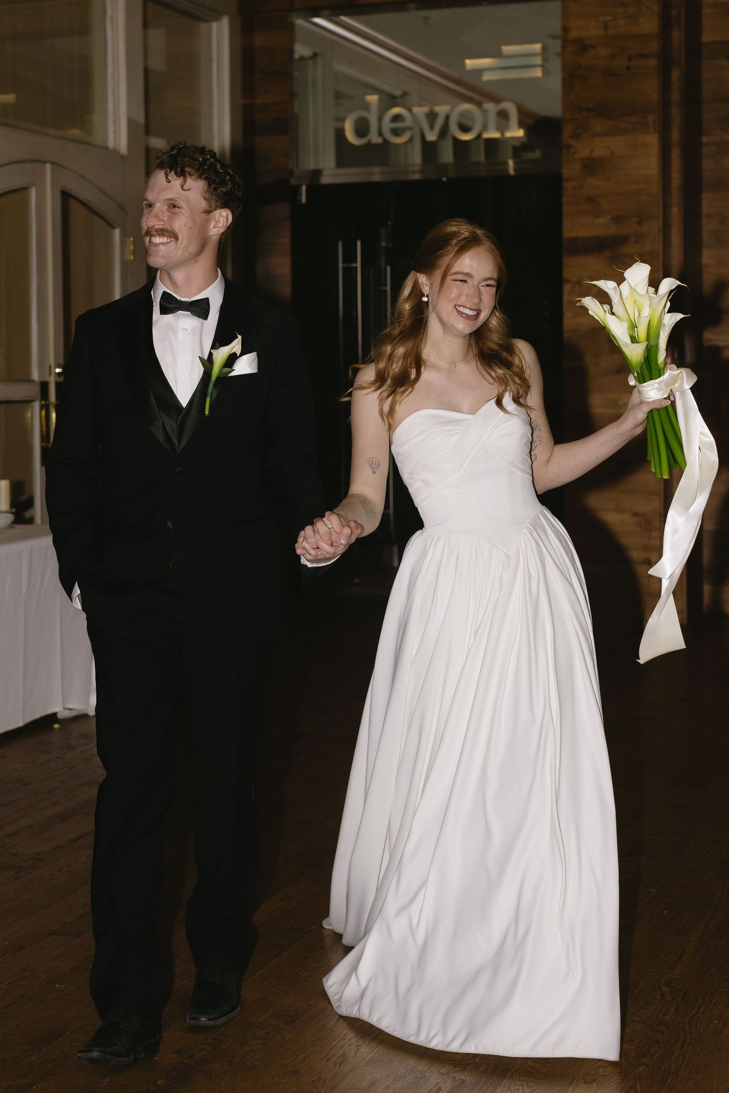 Wedding couple dances together in elegant indoor venue with wooden floors.