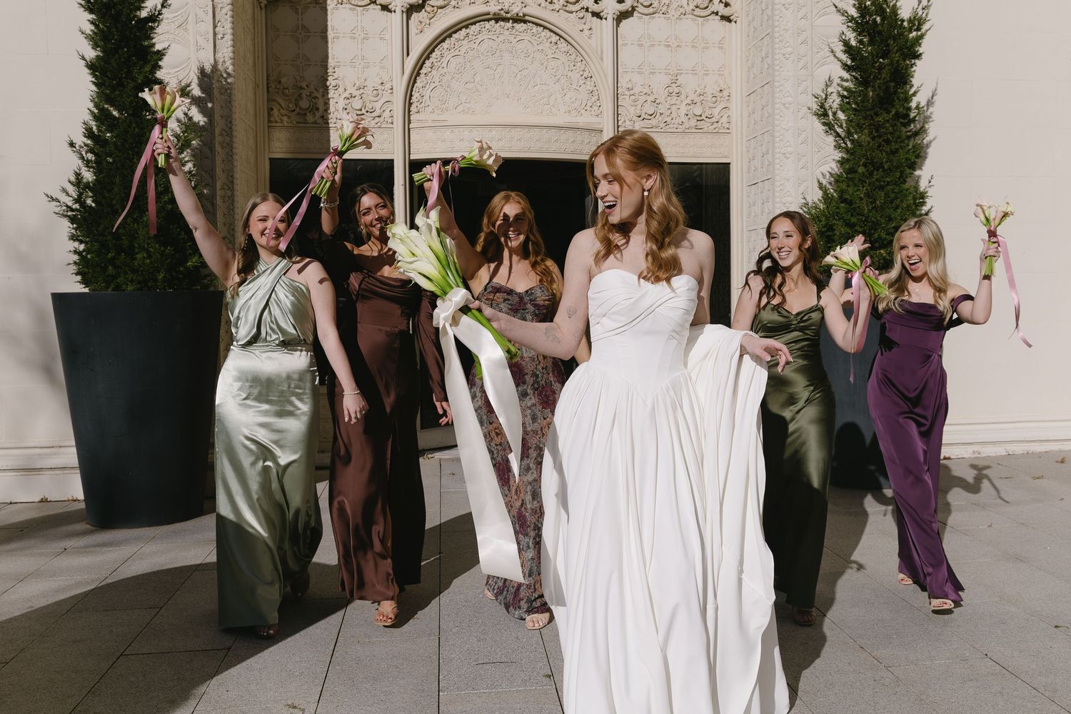 Wedding party celebrating with bridesmaids in purple and green dresses outside.