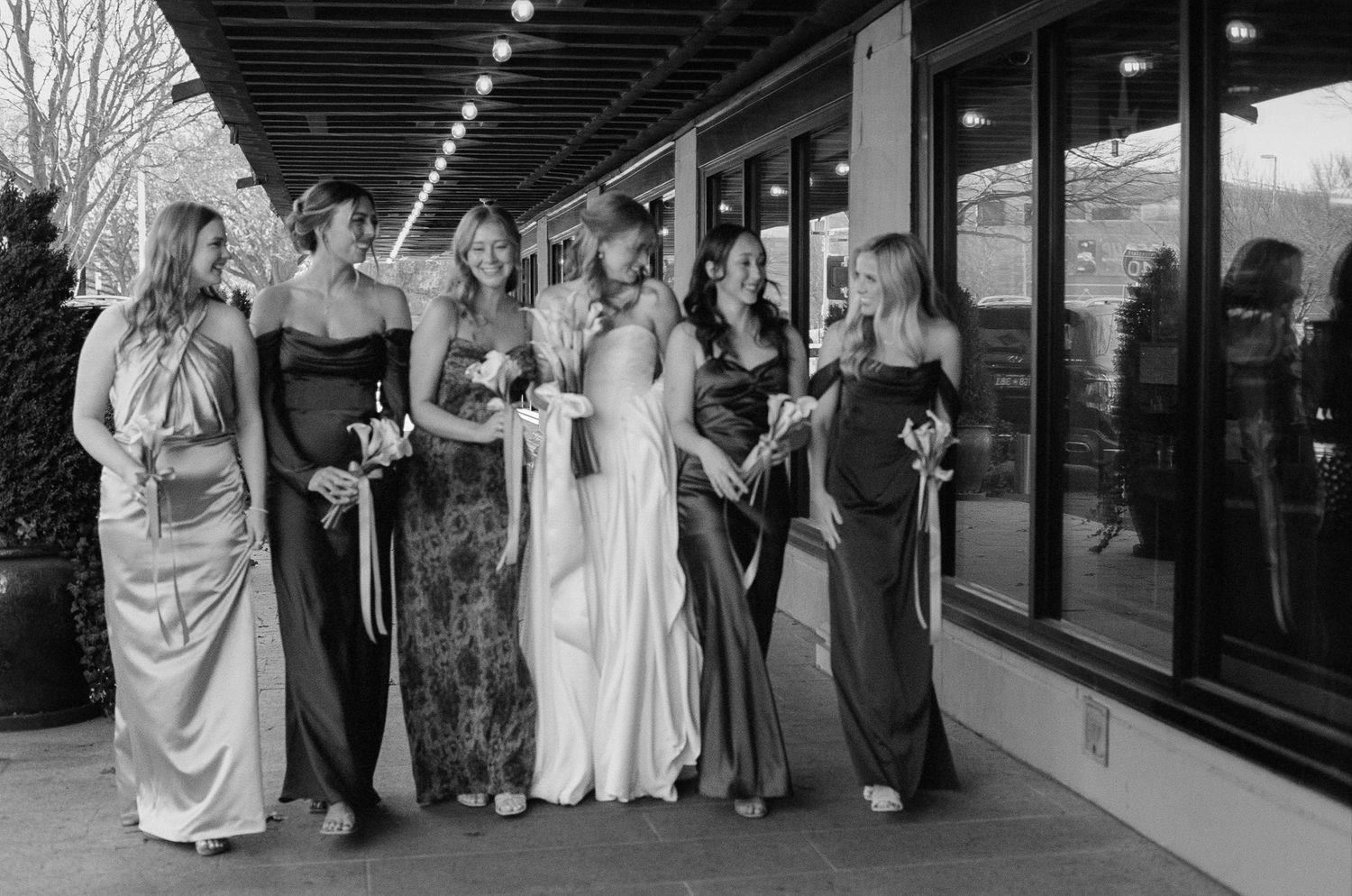 Wedding party members pose together outside a modern building with glass windows.