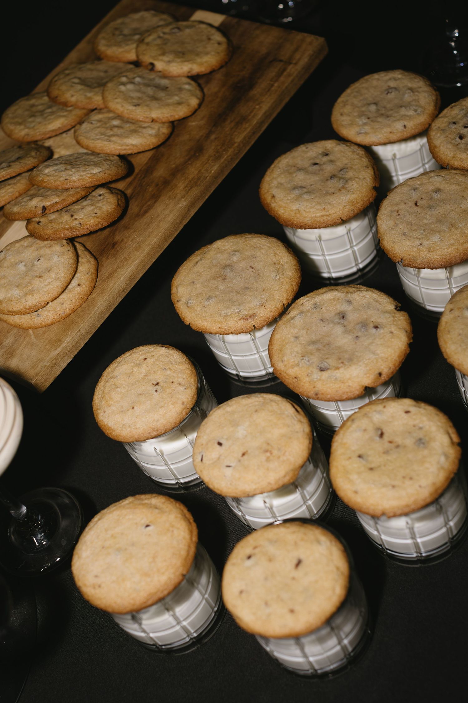 Freshly baked chocolate chip cookies arranged on a rustic wooden surface with white paper cups.