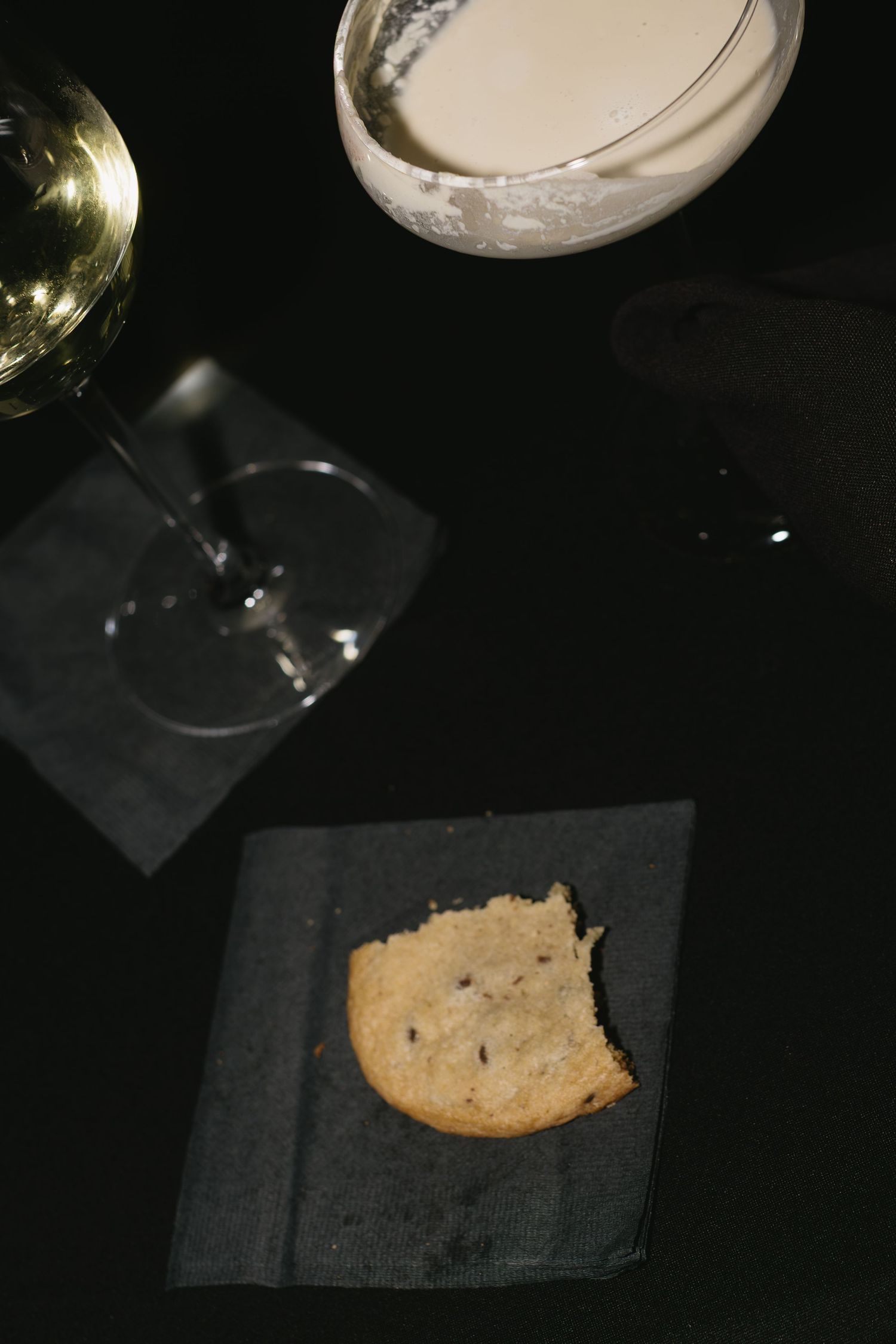 Wine glass and cookie on black napkin in low-light setting.