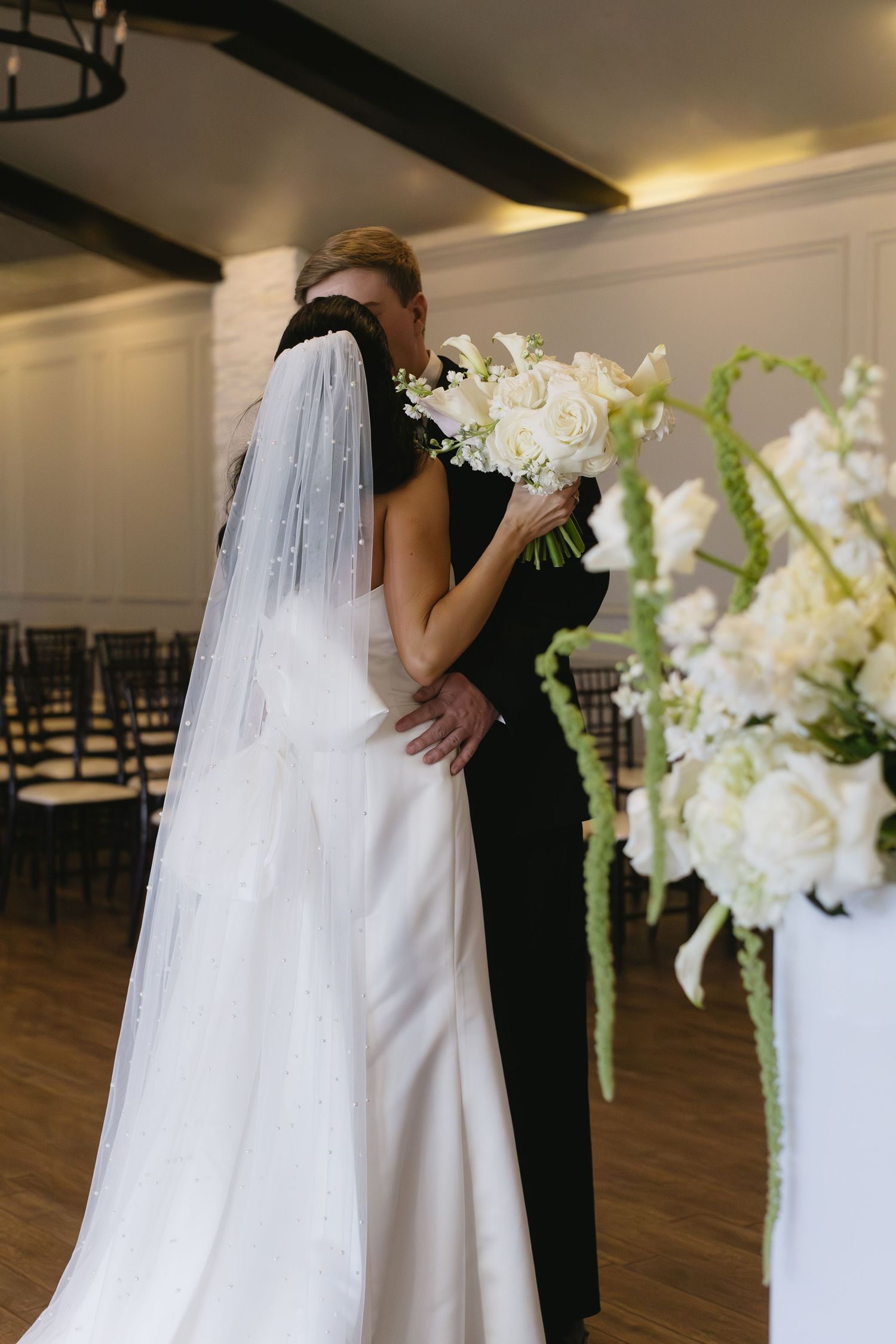 An intimate wedding moment captured indoors with white orchid decorations and hardwood floors.