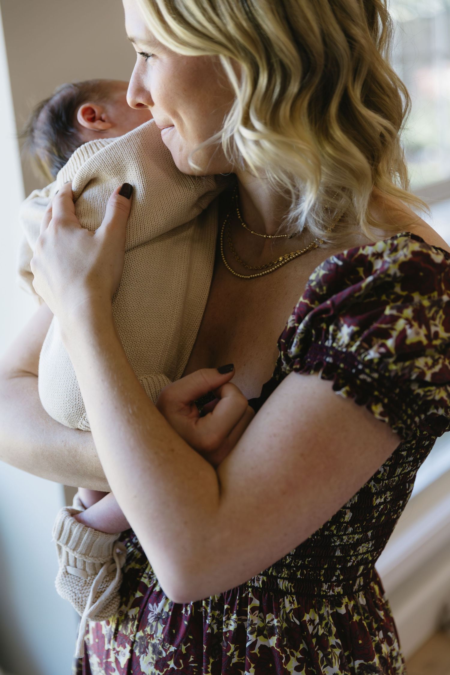 A tender moment captured in soft light as a floral dress-clad figure cradles a small infant.