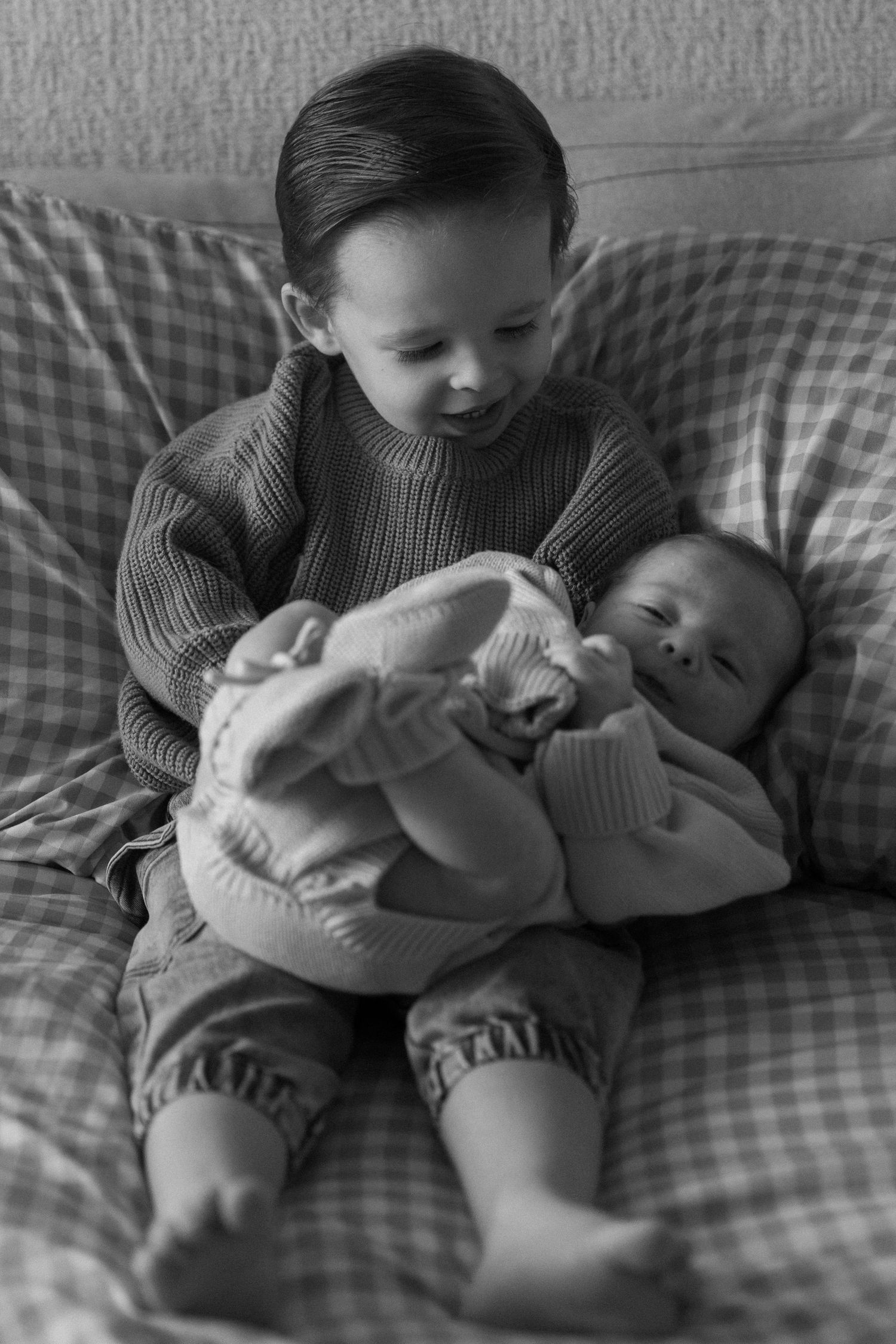 Two siblings share a sweet moment on a checkered couch as the older one holds the younger.