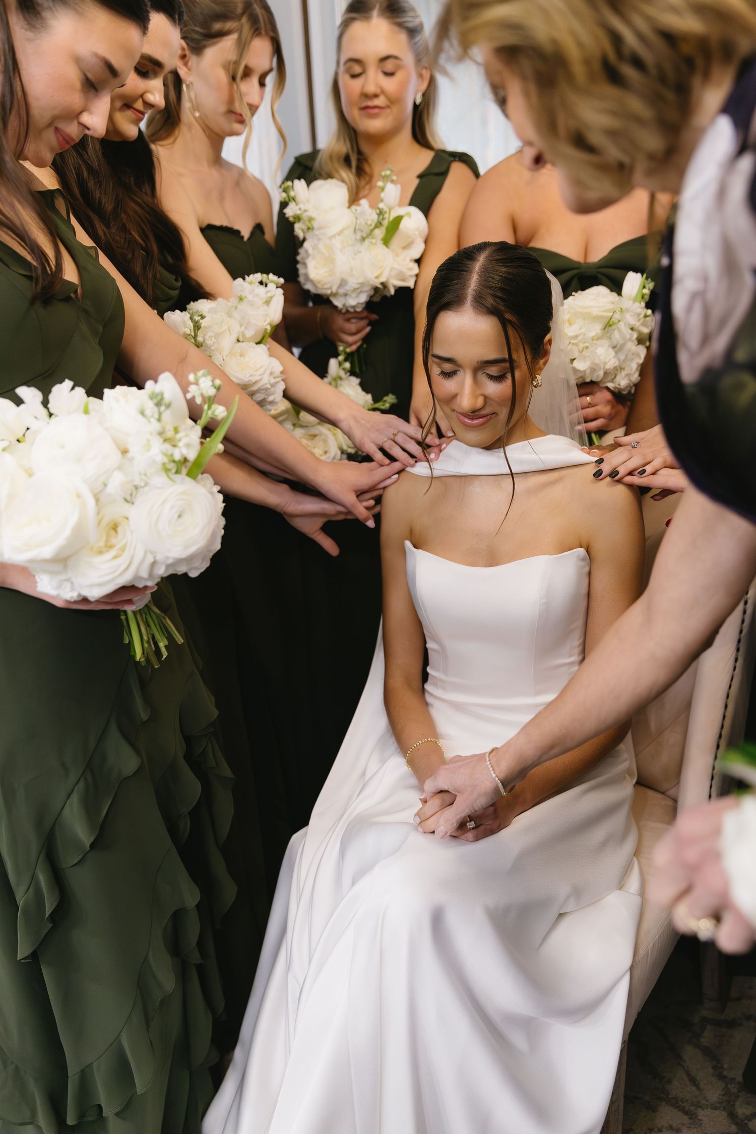 Wedding party gathers around bride in white dress with black-clad bridesmaids holding white bouquets.