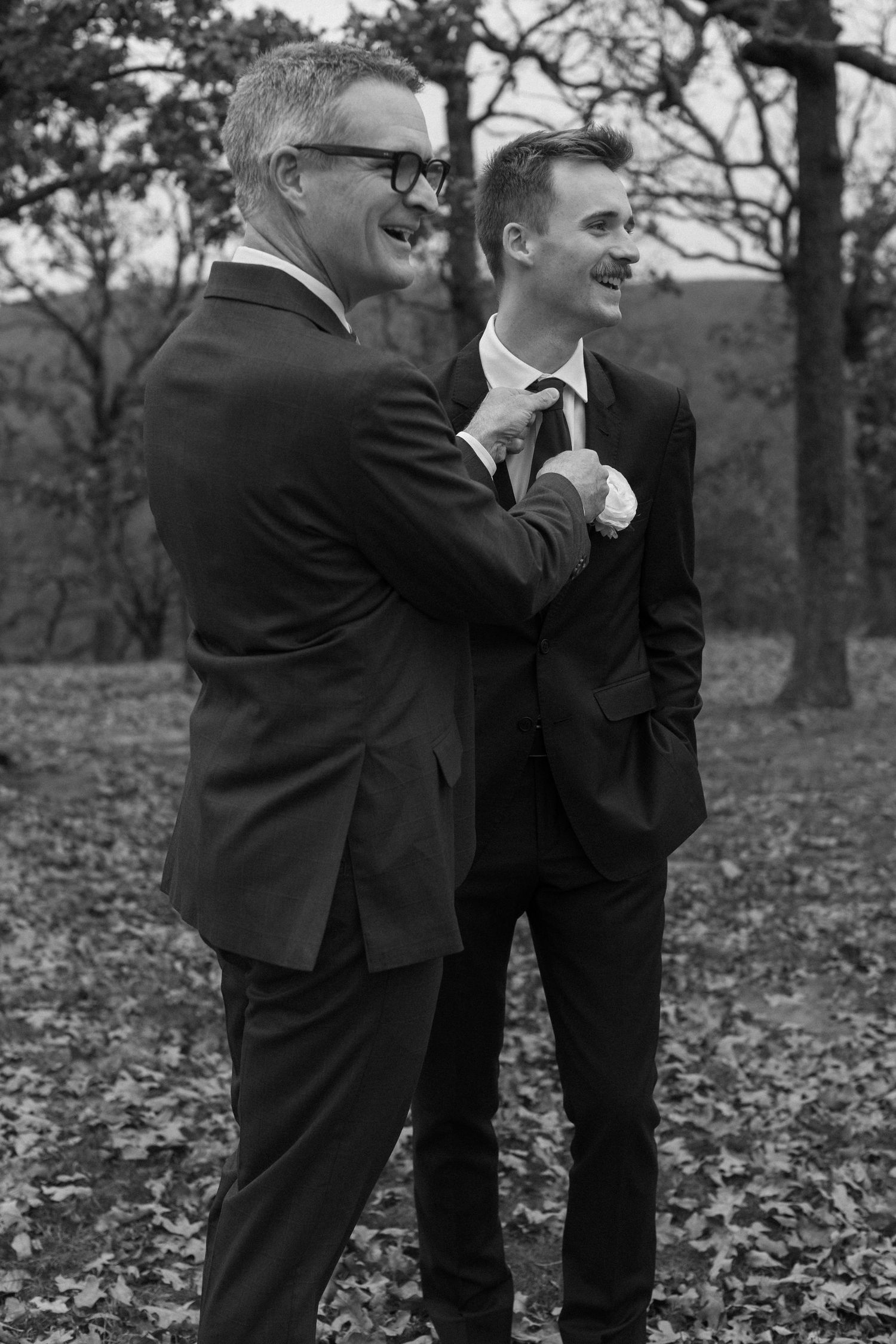 Groomsmen in dark suits playfully pose outdoors in autumn.