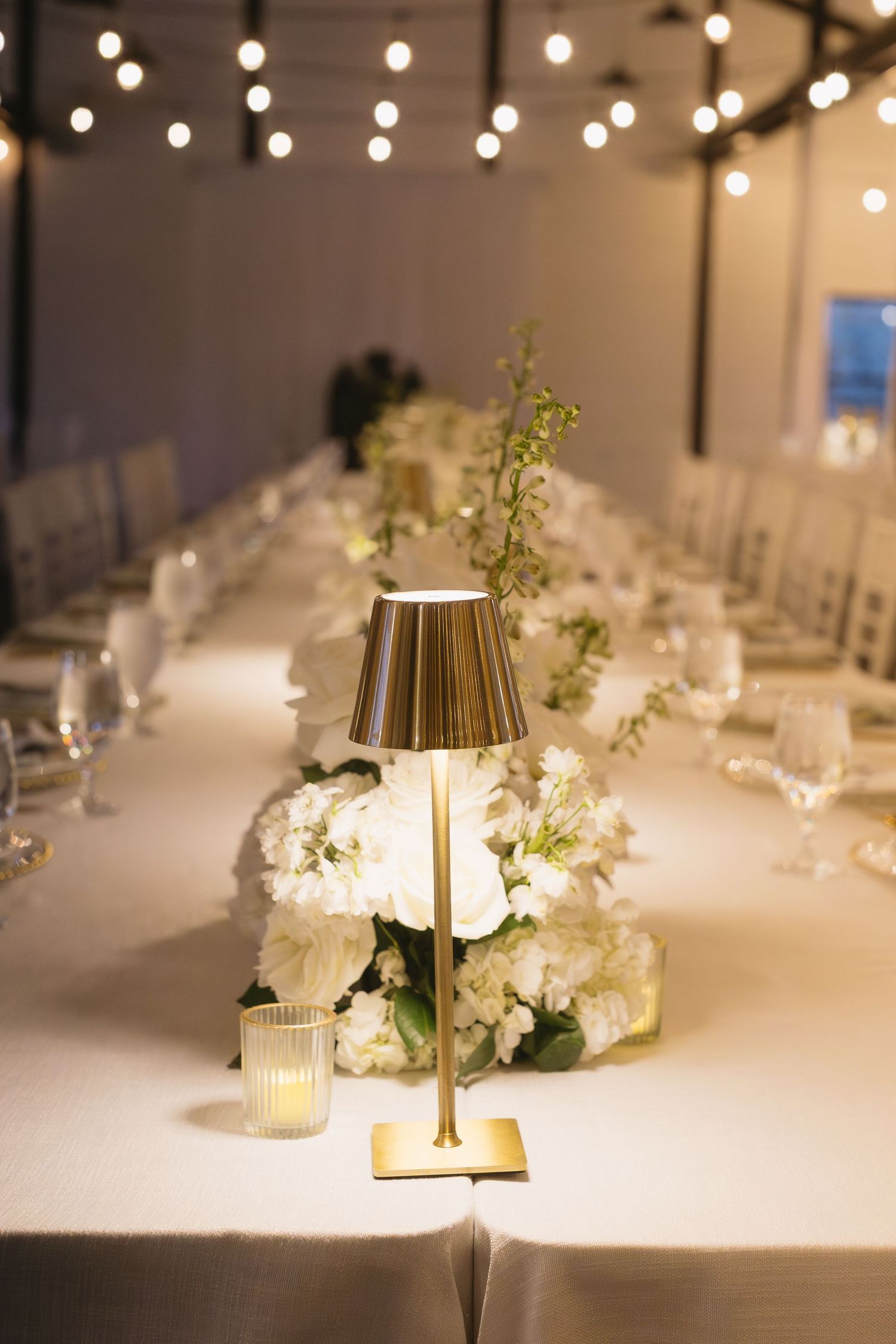 Elegant wedding reception table setting with gold lamp centerpieces and white floral arrangements.