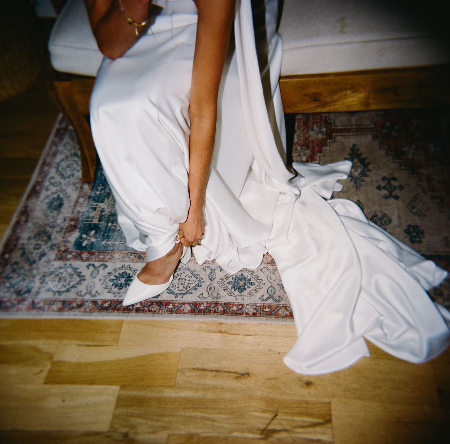 Close-up of a bride's white wedding dress and shoes on a patterned rug.