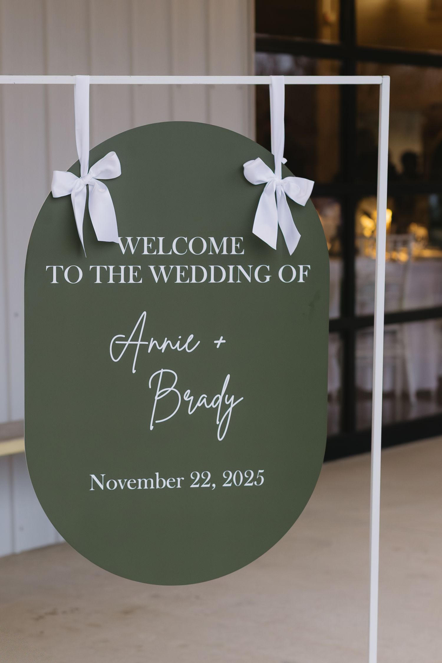 A sage green welcome sign with white bows displays wedding details for Annie and Brady's November celebration.