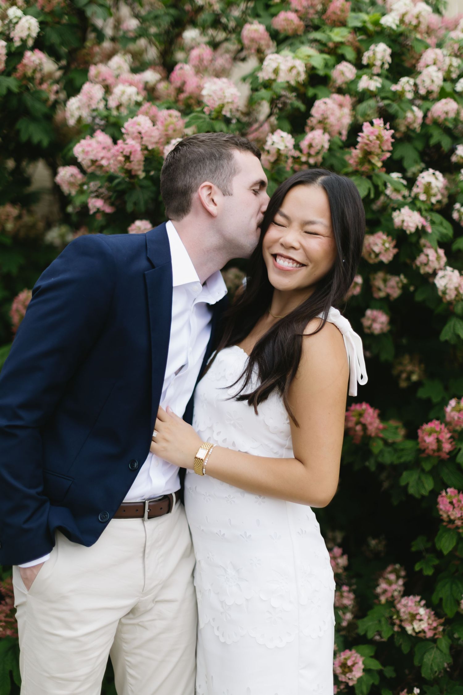 A couple shares romantic moments against a backdrop of blooming pink roses in a garden setting.