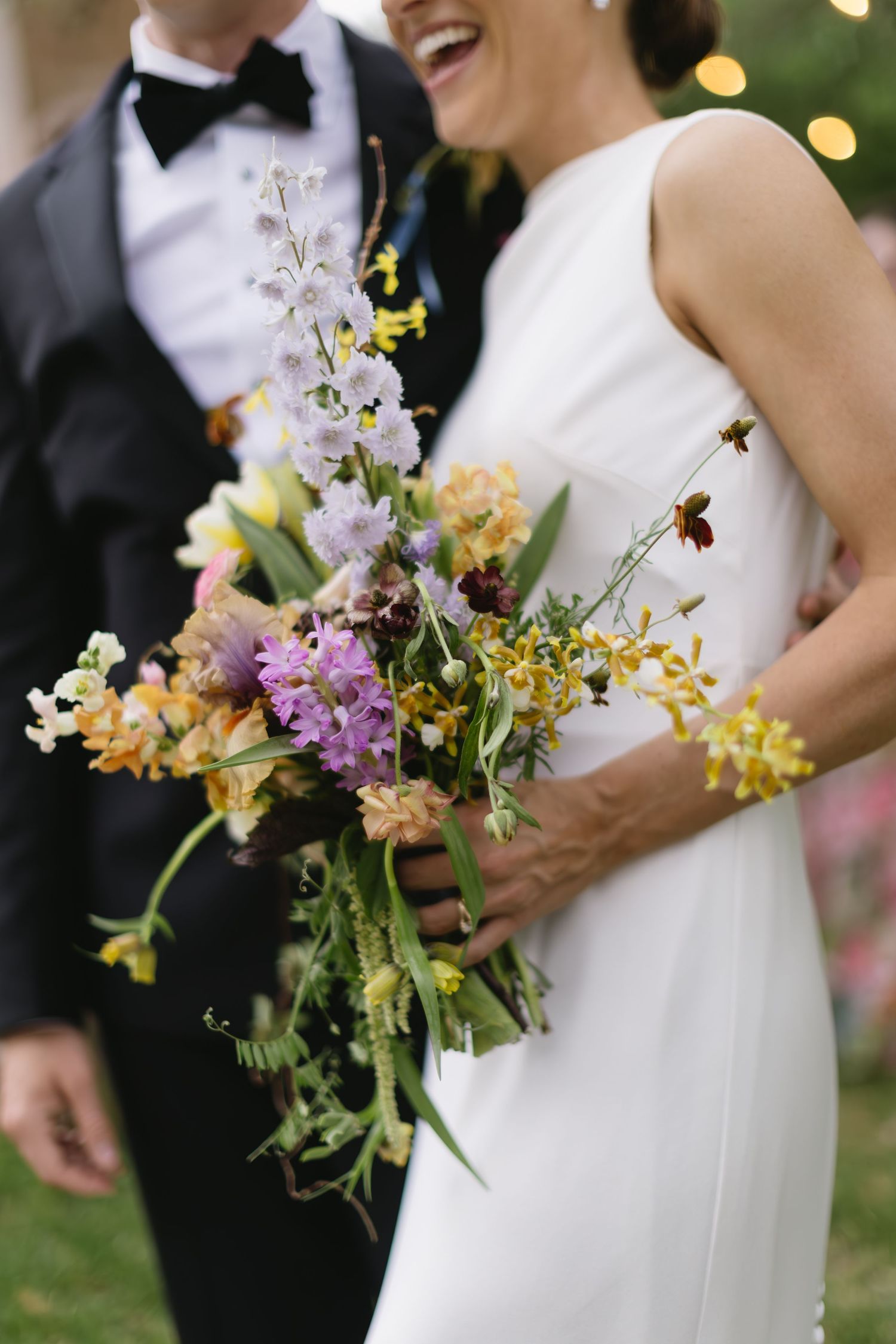 Close up view of colorful wildflower bouquets with yellow and purple blooms against a white dress.