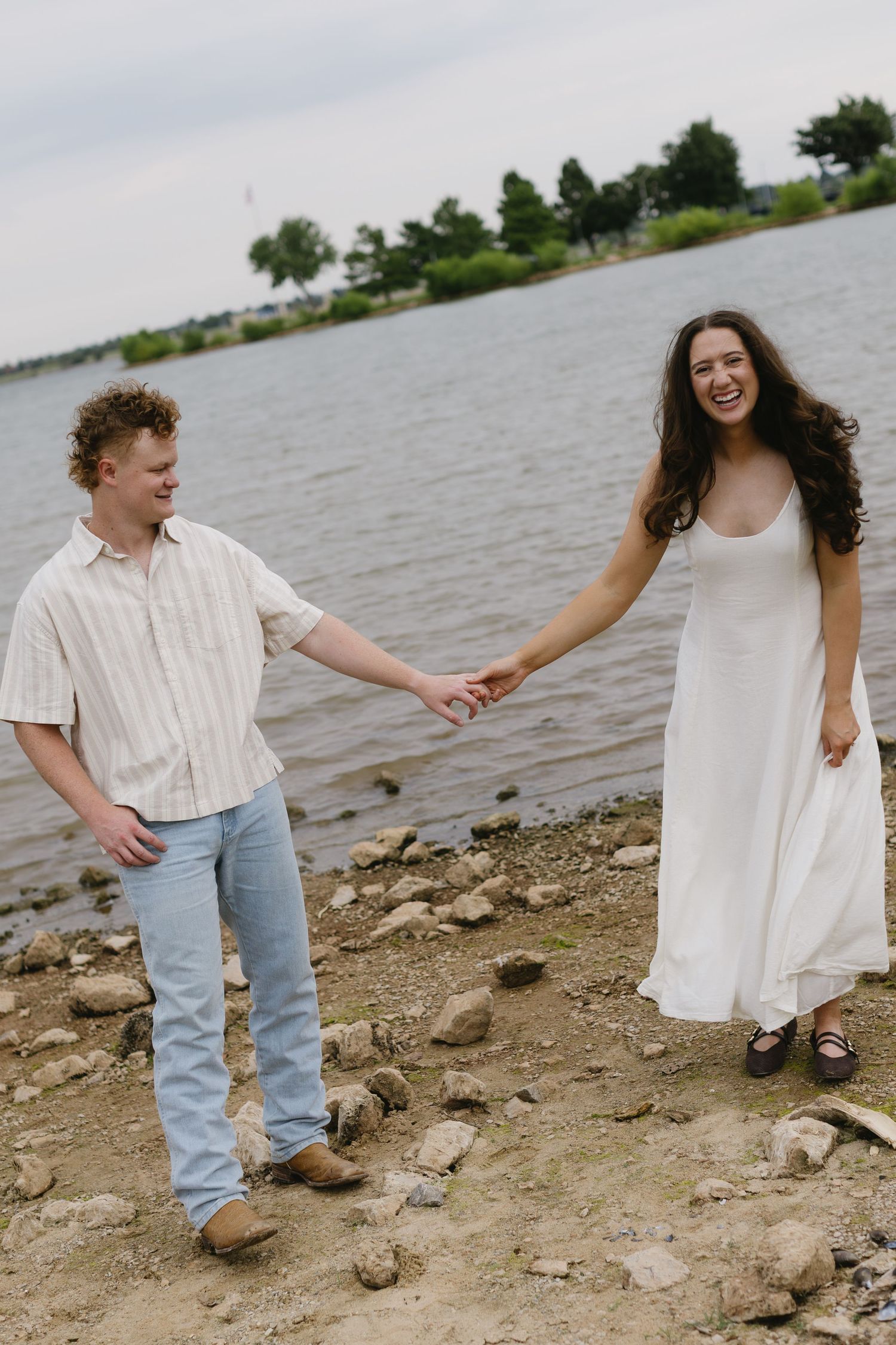 Playful couple holding hands while exploring rocky lakeside terrain.