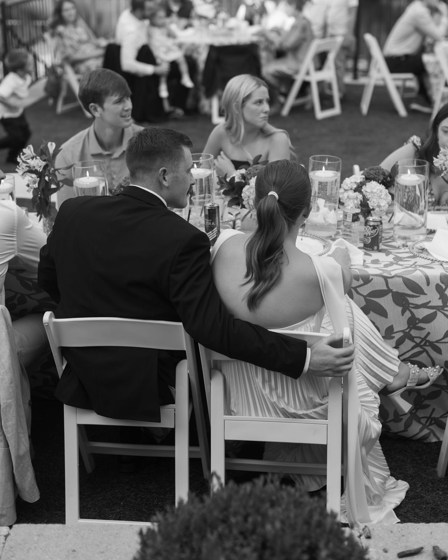 A black and white photo of a reception dinner with guests seated at decorated tables outdoors.