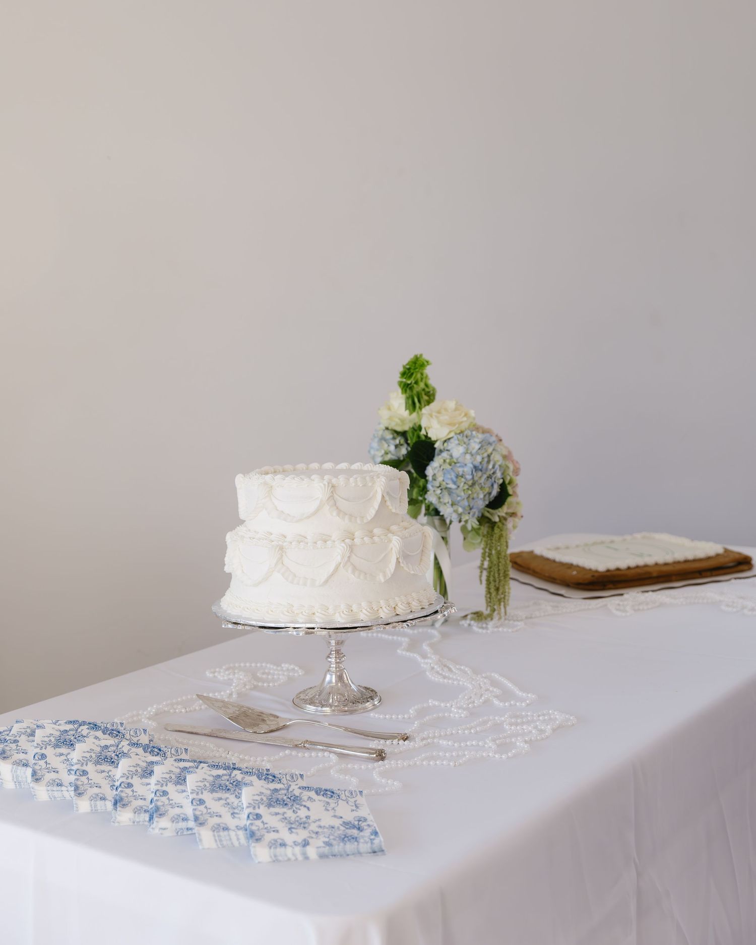 White wedding cake and delicate floral arrangements displayed on a lace-covered table.