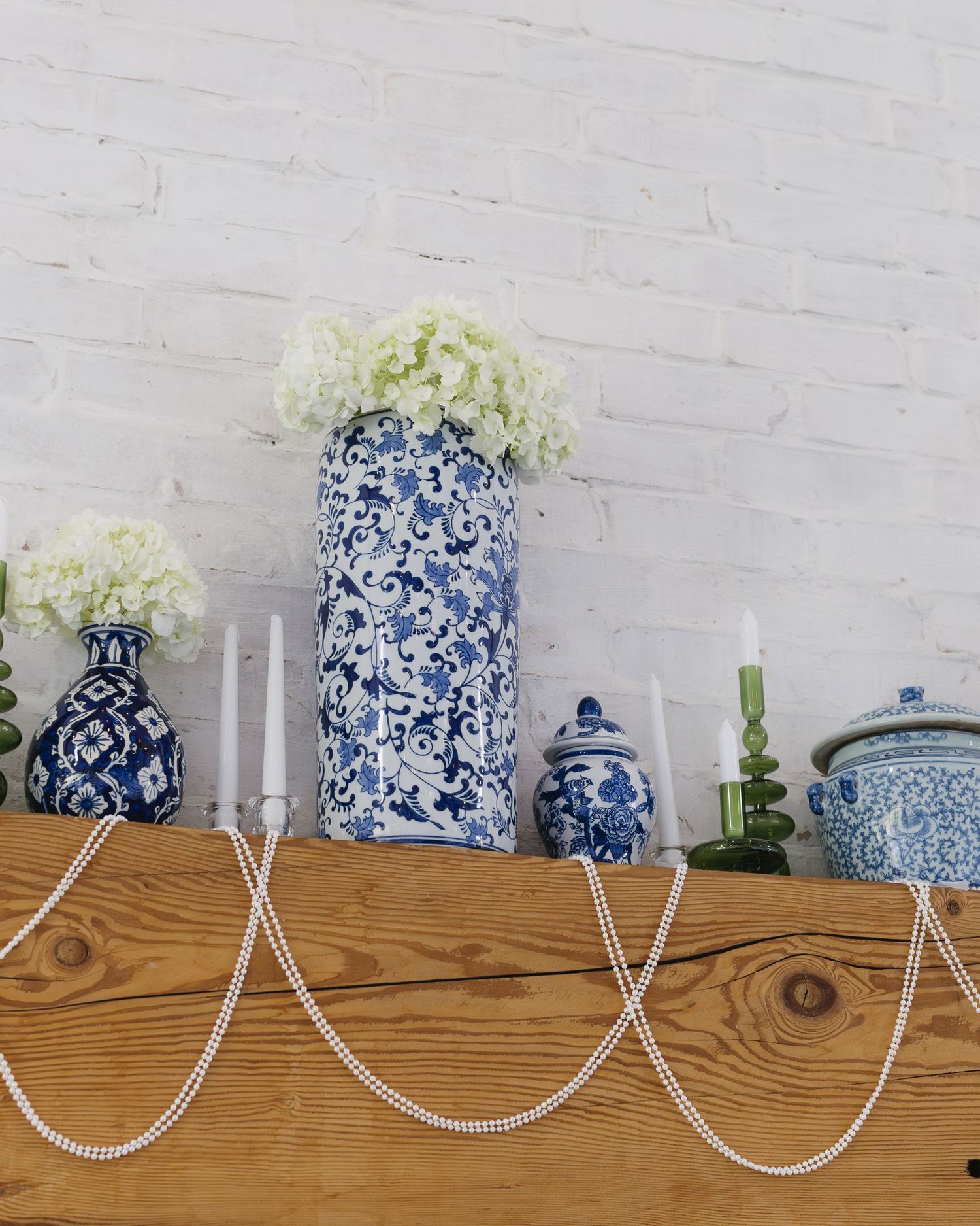 Blue and white chinoiserie vases with hydrangeas displayed on a wooden shelf with white string lights.