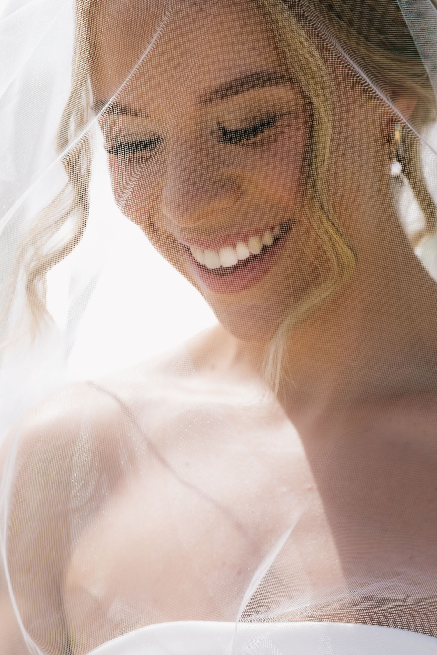 Close-up portrait of a radiant smiling bride with soft lighting and delicate veil creating an ethereal atmosphere.