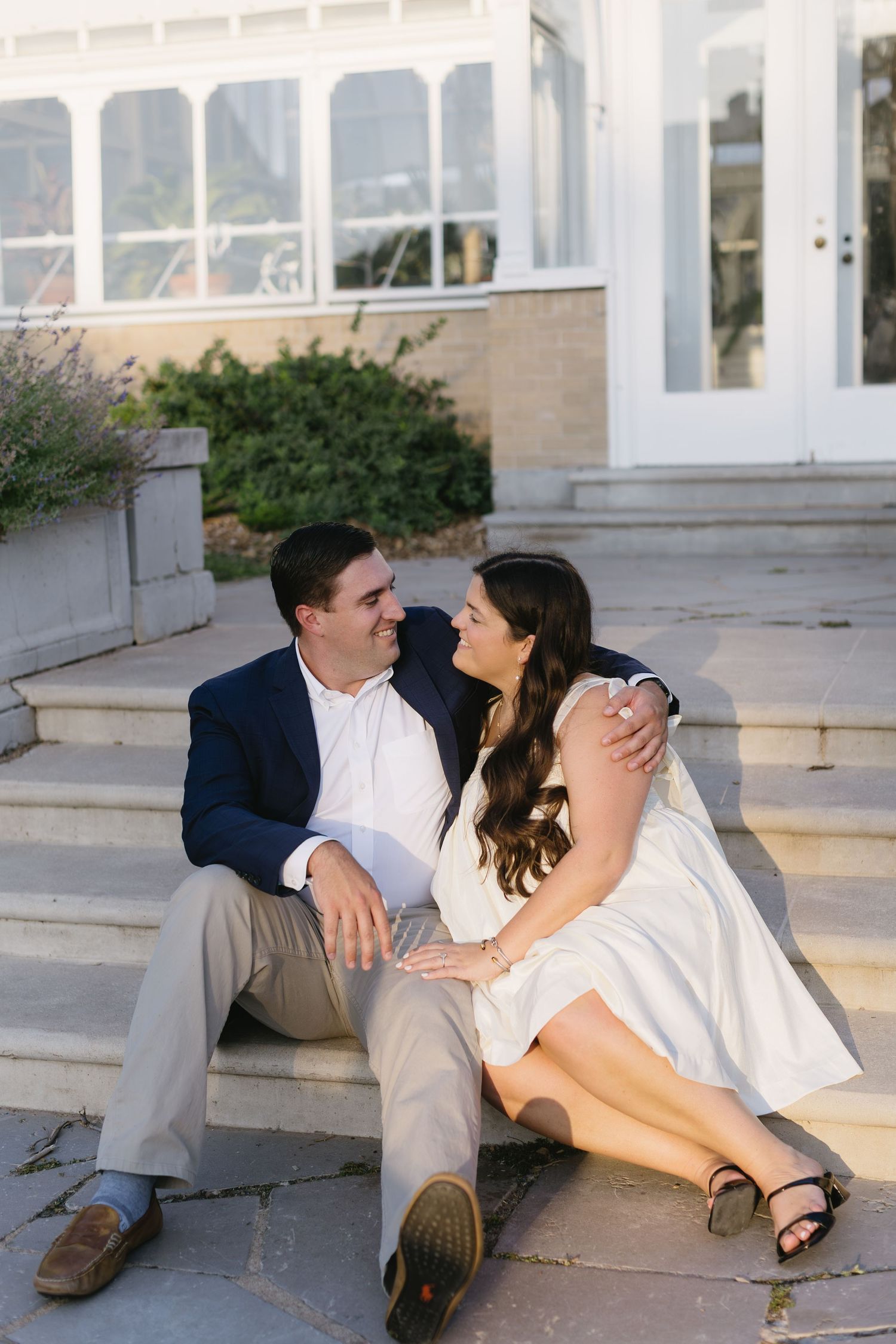 A couple relaxes and poses playfully on concrete steps in formal wear.
