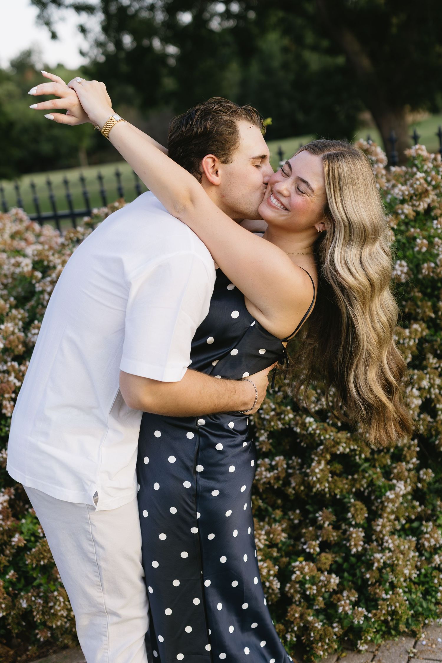 Romantic embrace near flowering bushes in a garden setting.