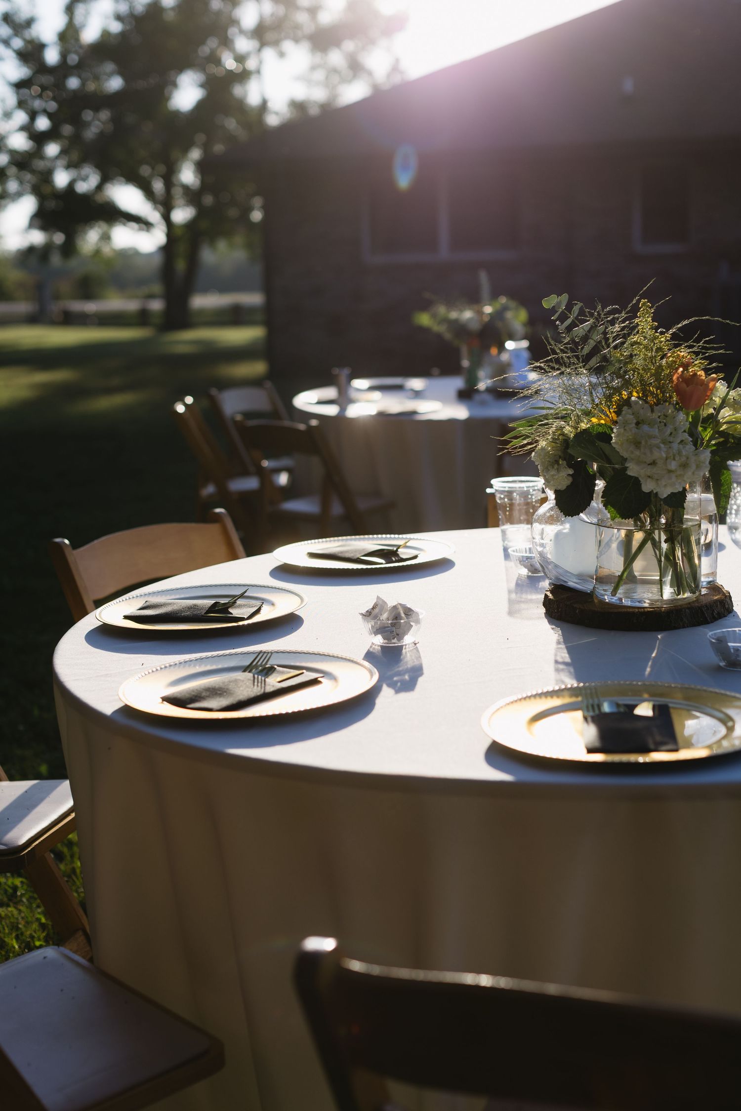 Wedding reception table settings with white linens and natural lighting.