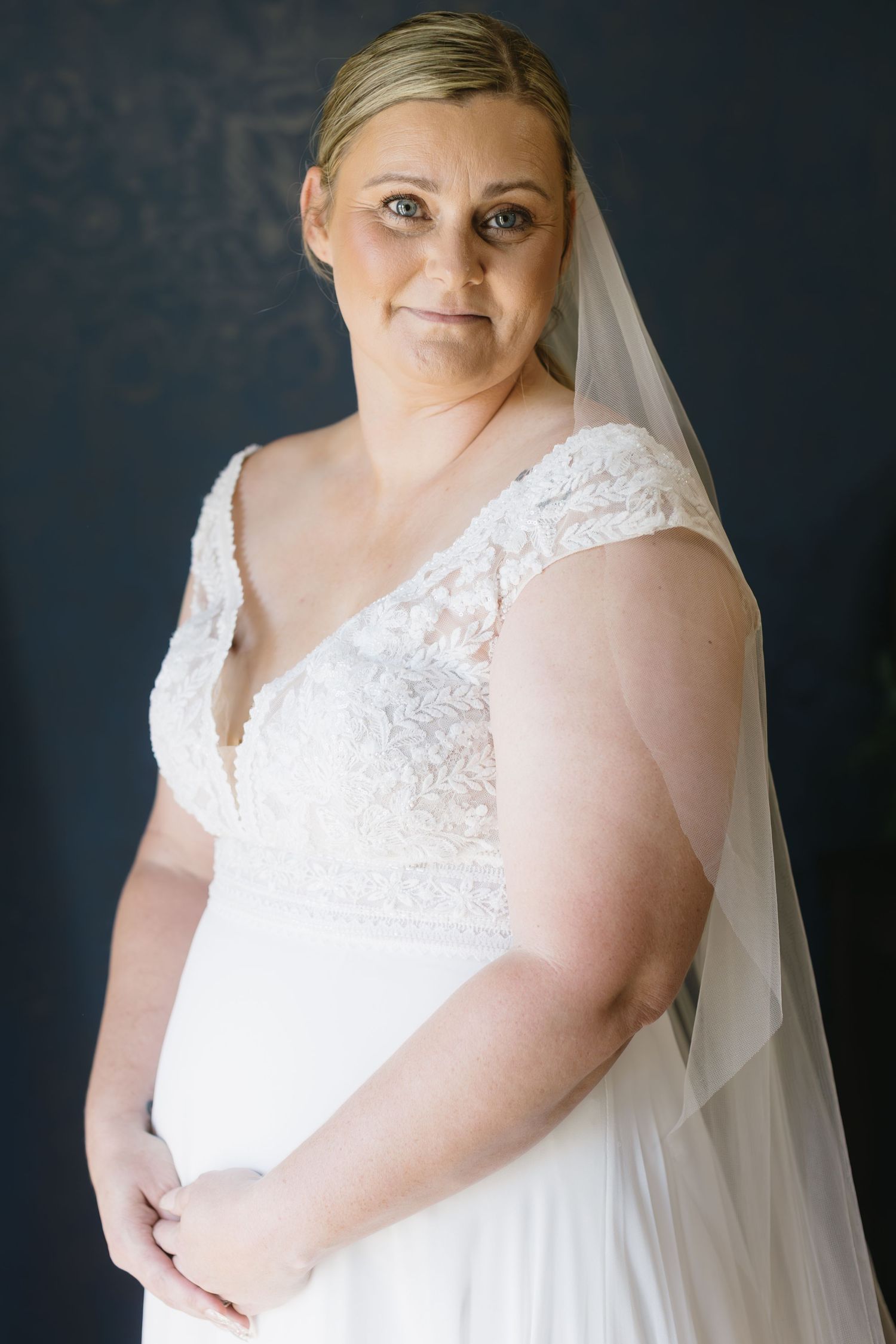 Bridal portraits against a dark backdrop showcase an elegant white lace wedding dress and flowing veil.