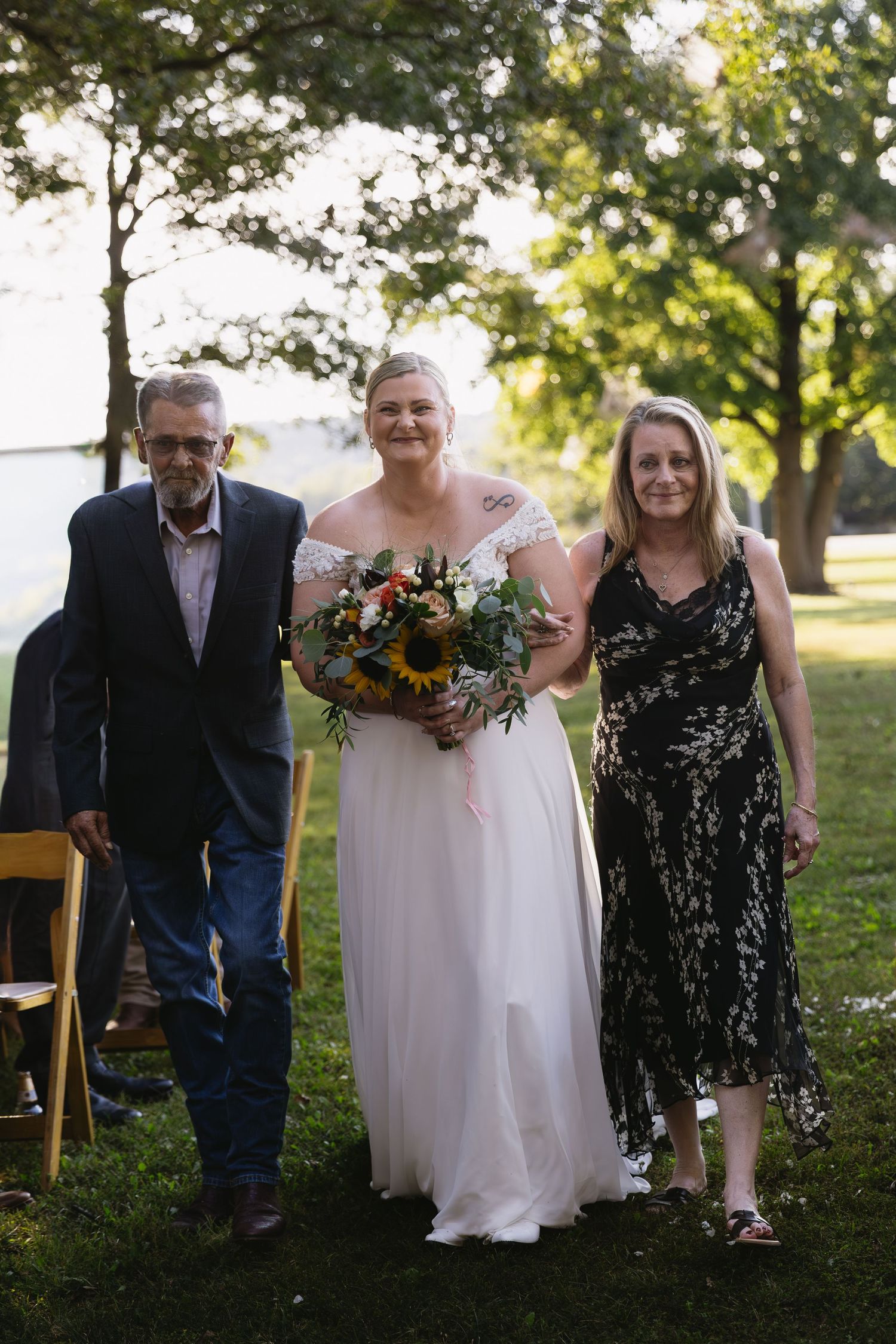 Wedding party poses together on grassy lawn with sunflowers and formal attire.