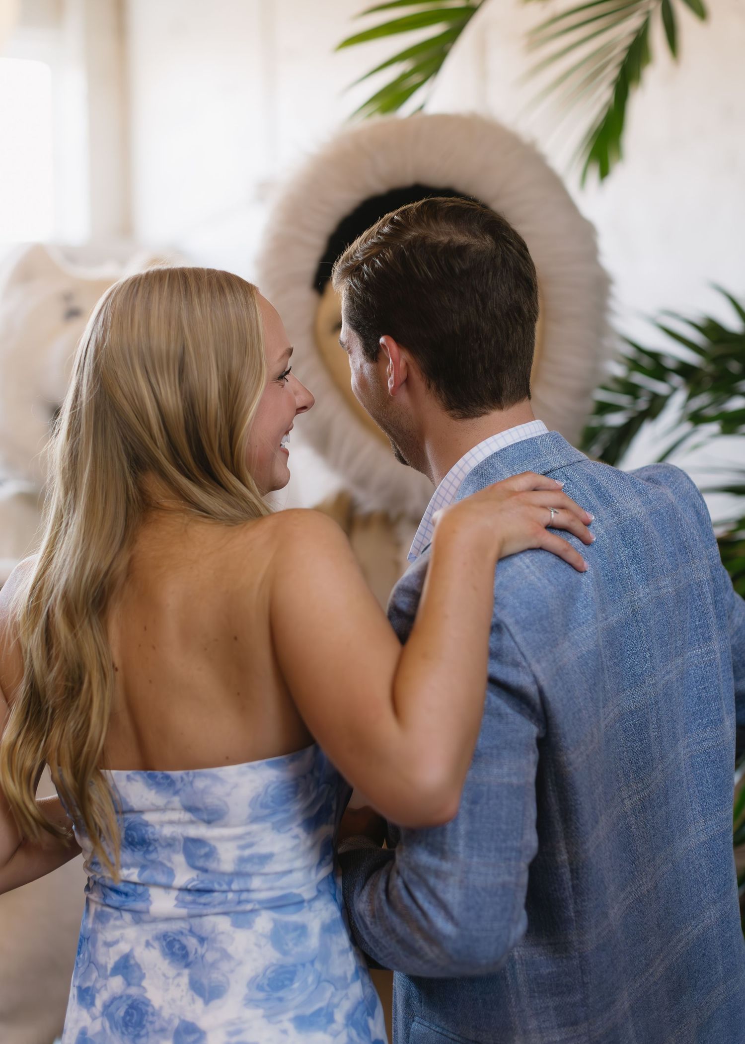 A couple in blue and white attire posing together in a tropical setting with palm leaves.