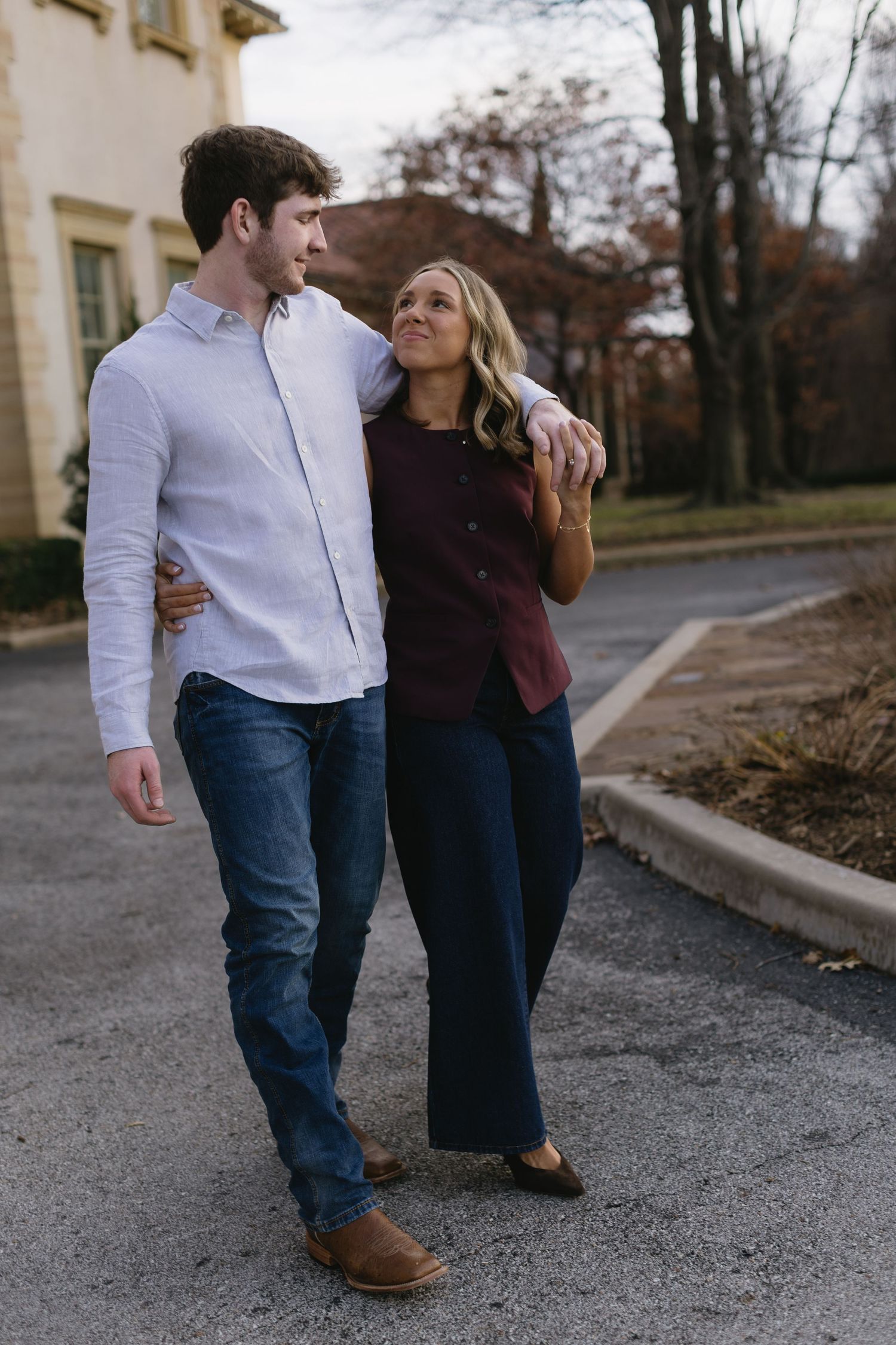 A couple walking together and smiling on a fall day in front of a historic building.