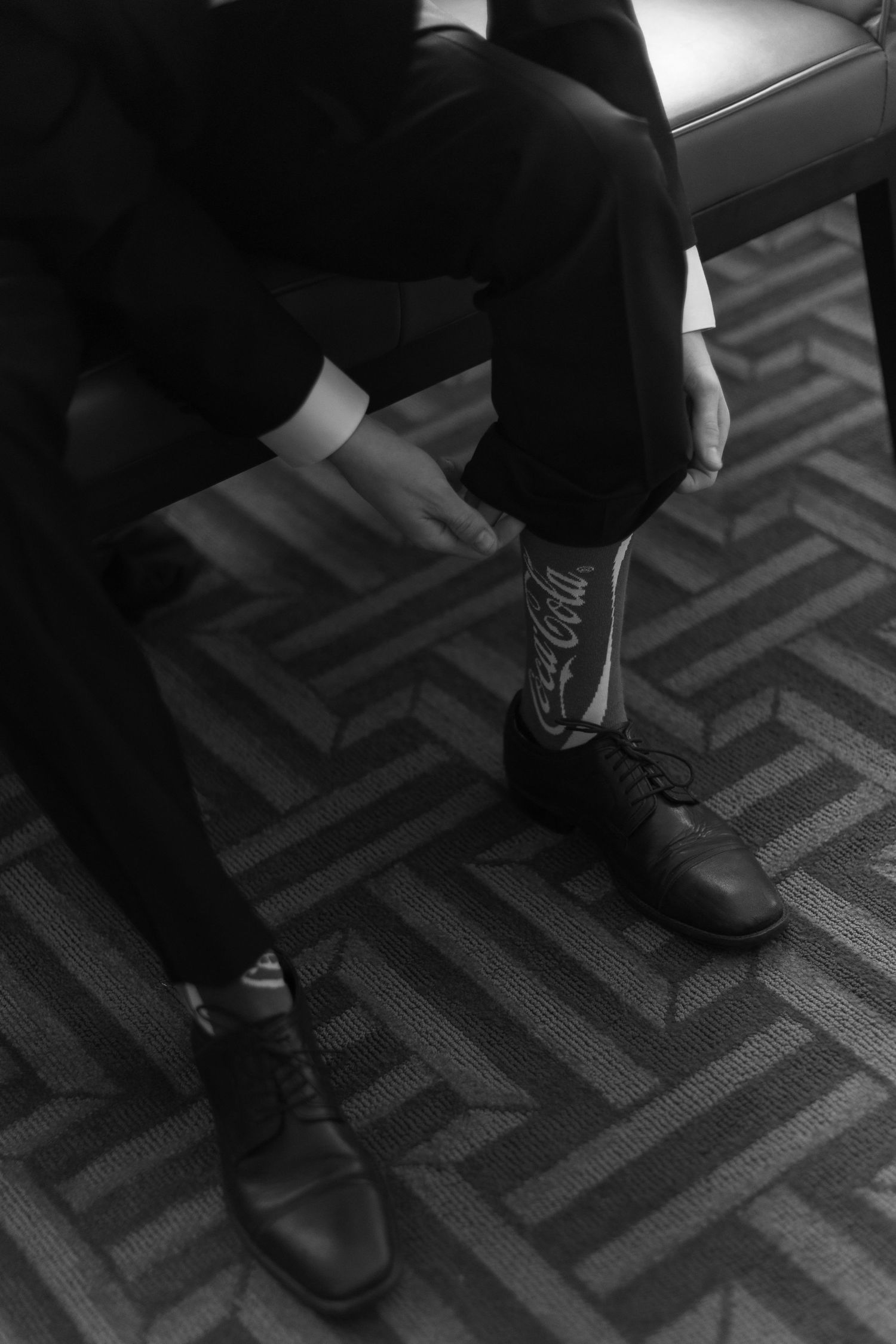 Black and white detail of formal dress shoes on patterned carpet.