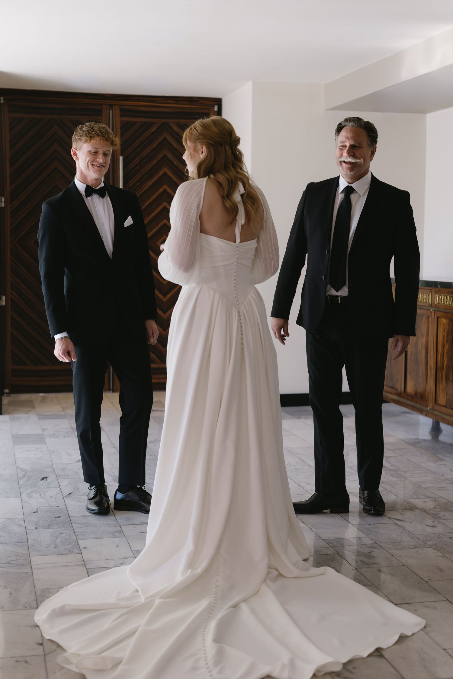 Wedding party in formal attire with flowing white gown and black tuxedos.