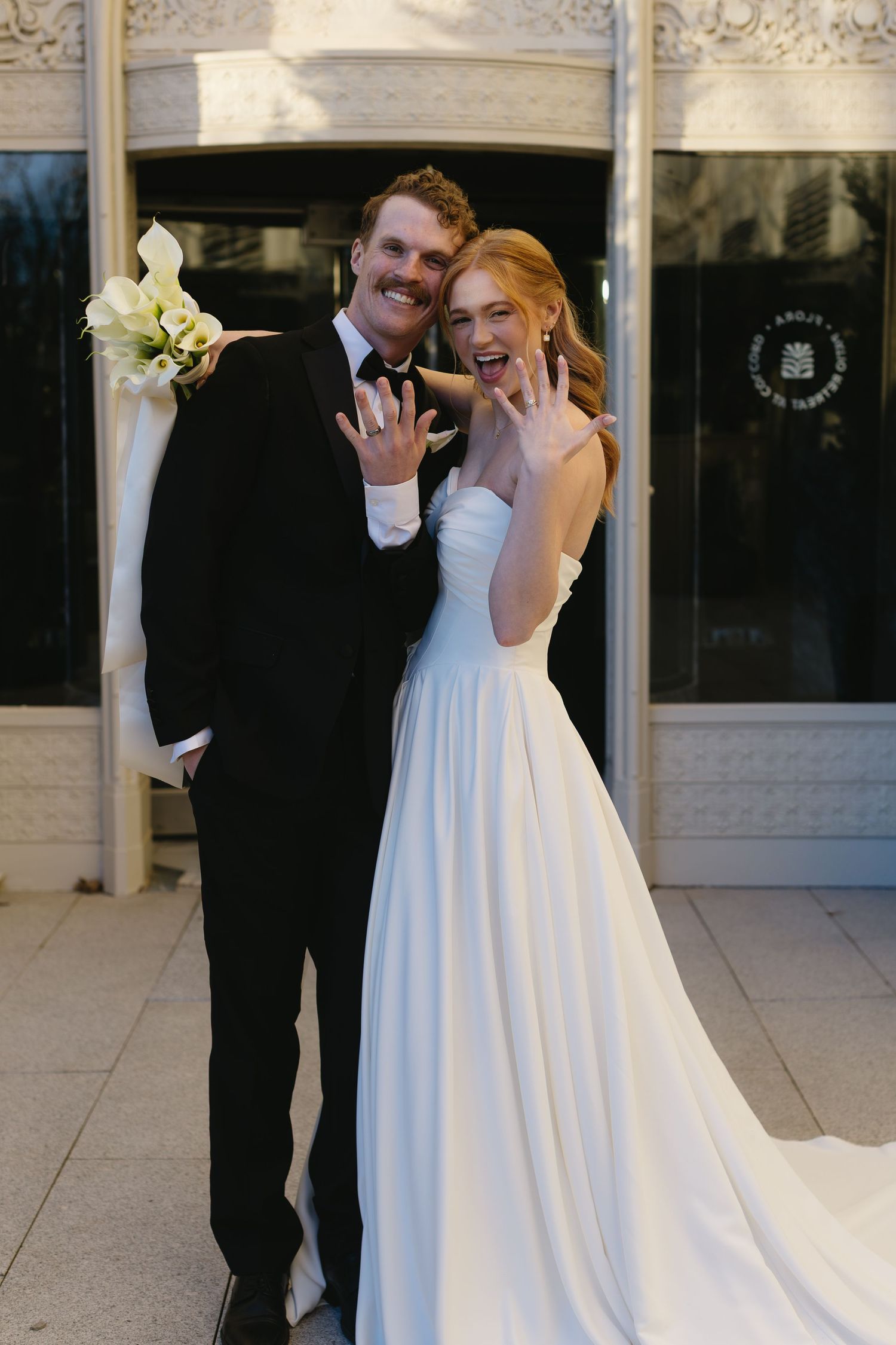 Romantic wedding moment captured against decorative white stone facade.