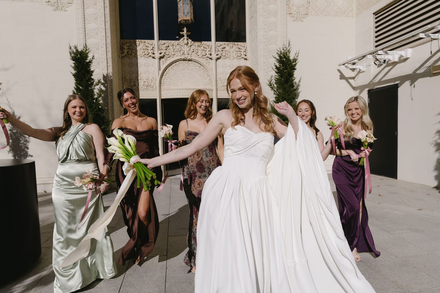Wedding party members laughing and celebrating outside a modern building.