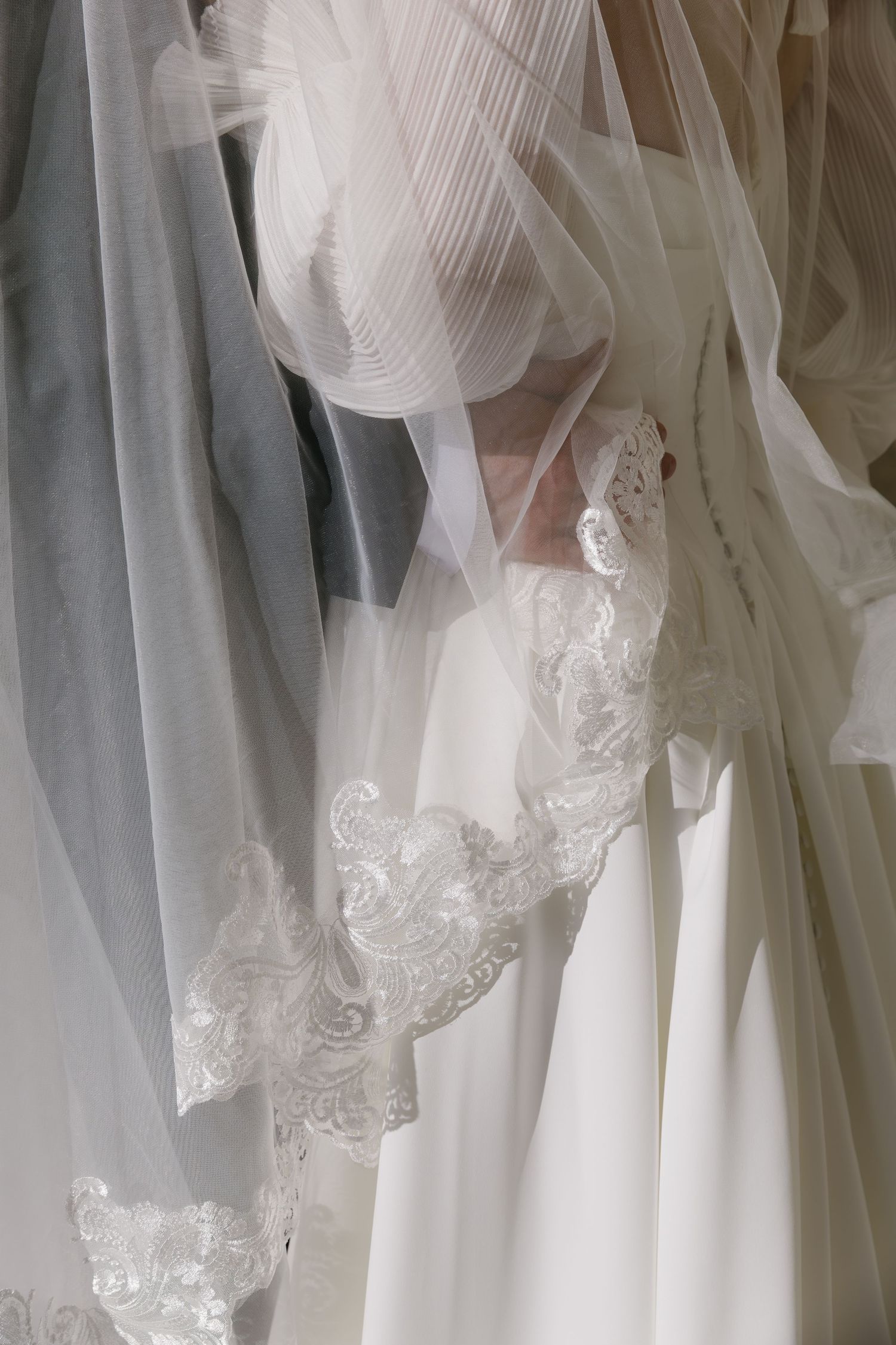 Close-up details of delicate white lace and tulle on a wedding dress hanging.