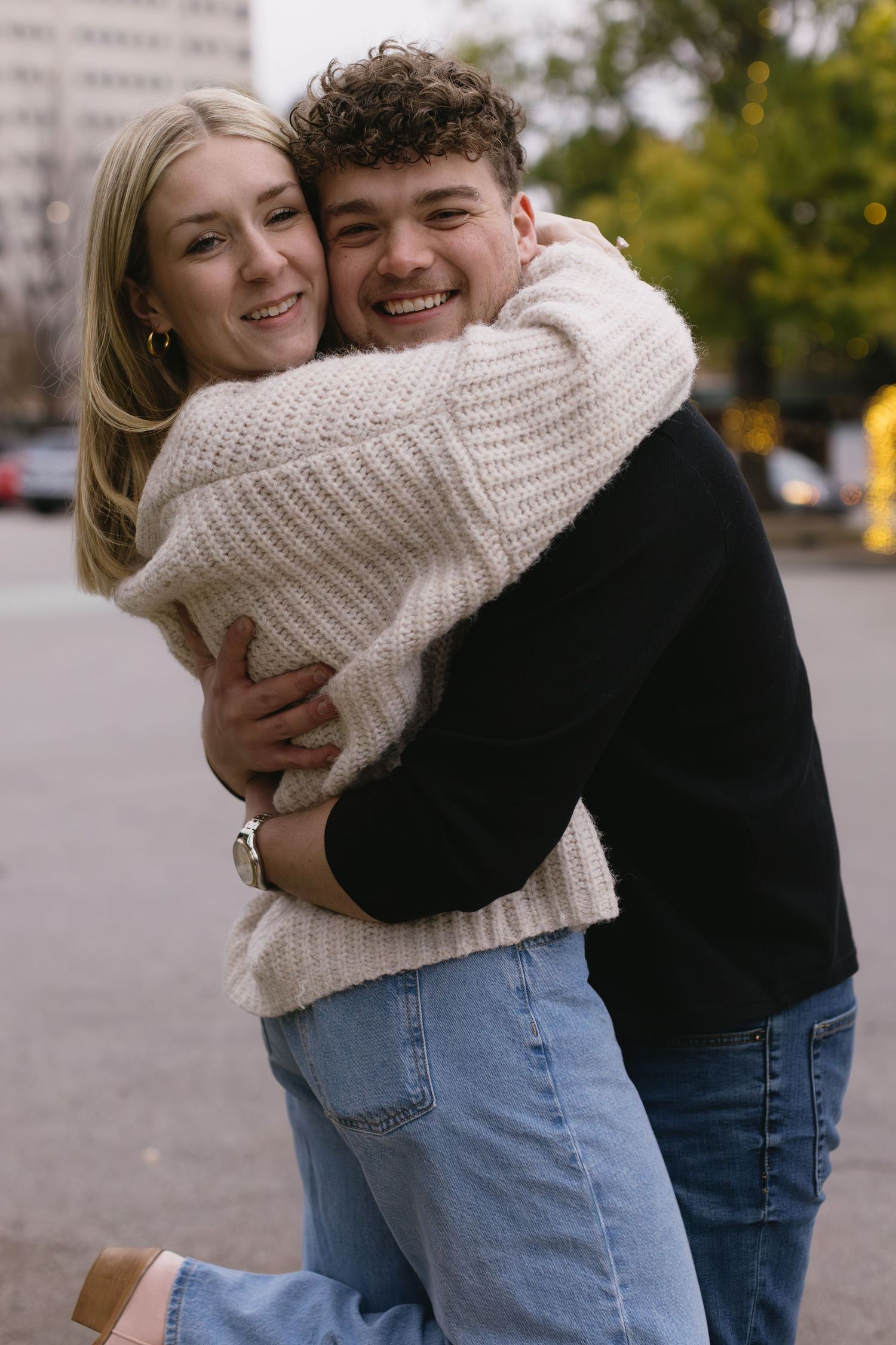 A couple in matching jeans embrace and laugh together during an autumn photoshoot.