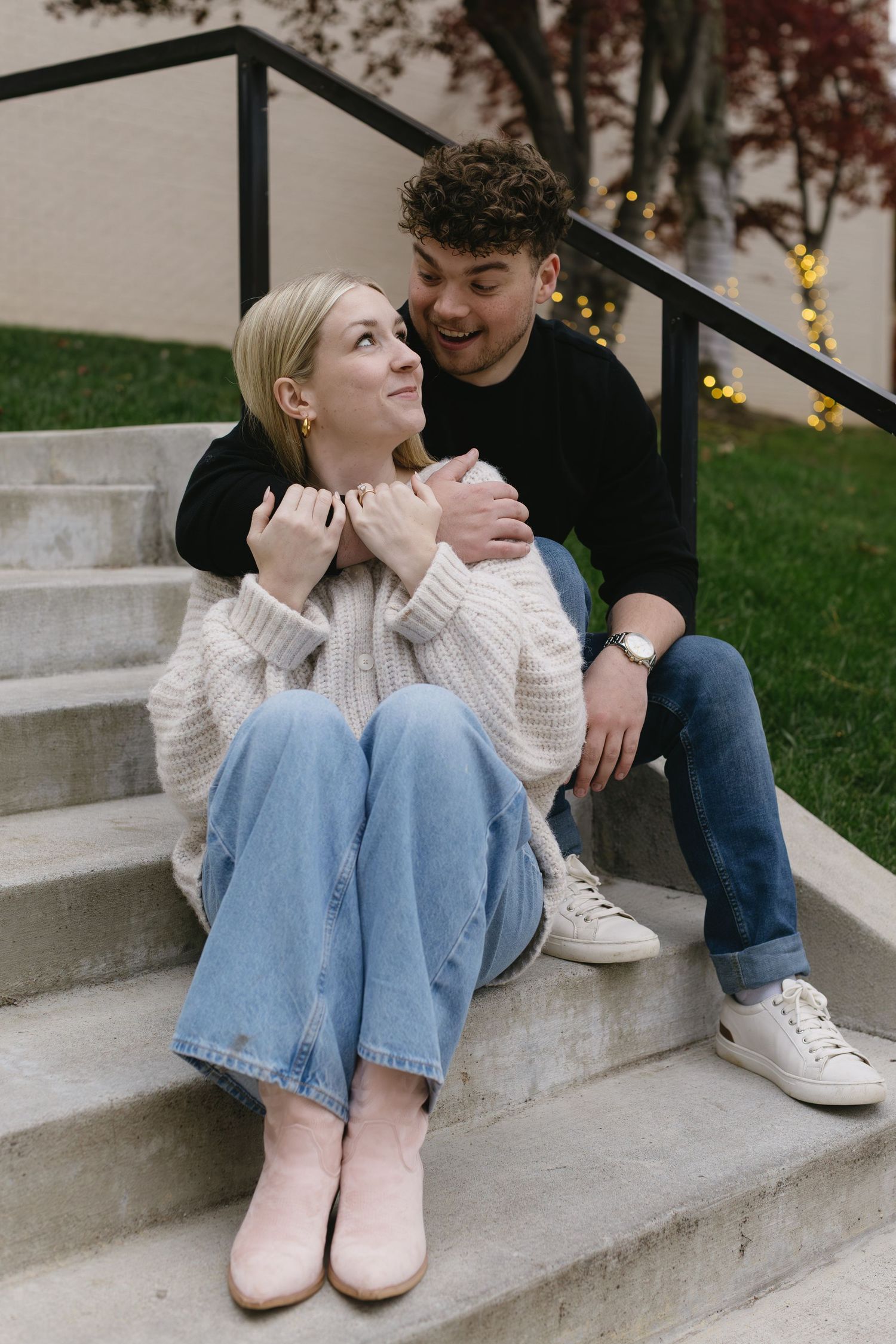 A couple sitting on concrete steps wearing casual outfits with a white sweater and dark top.