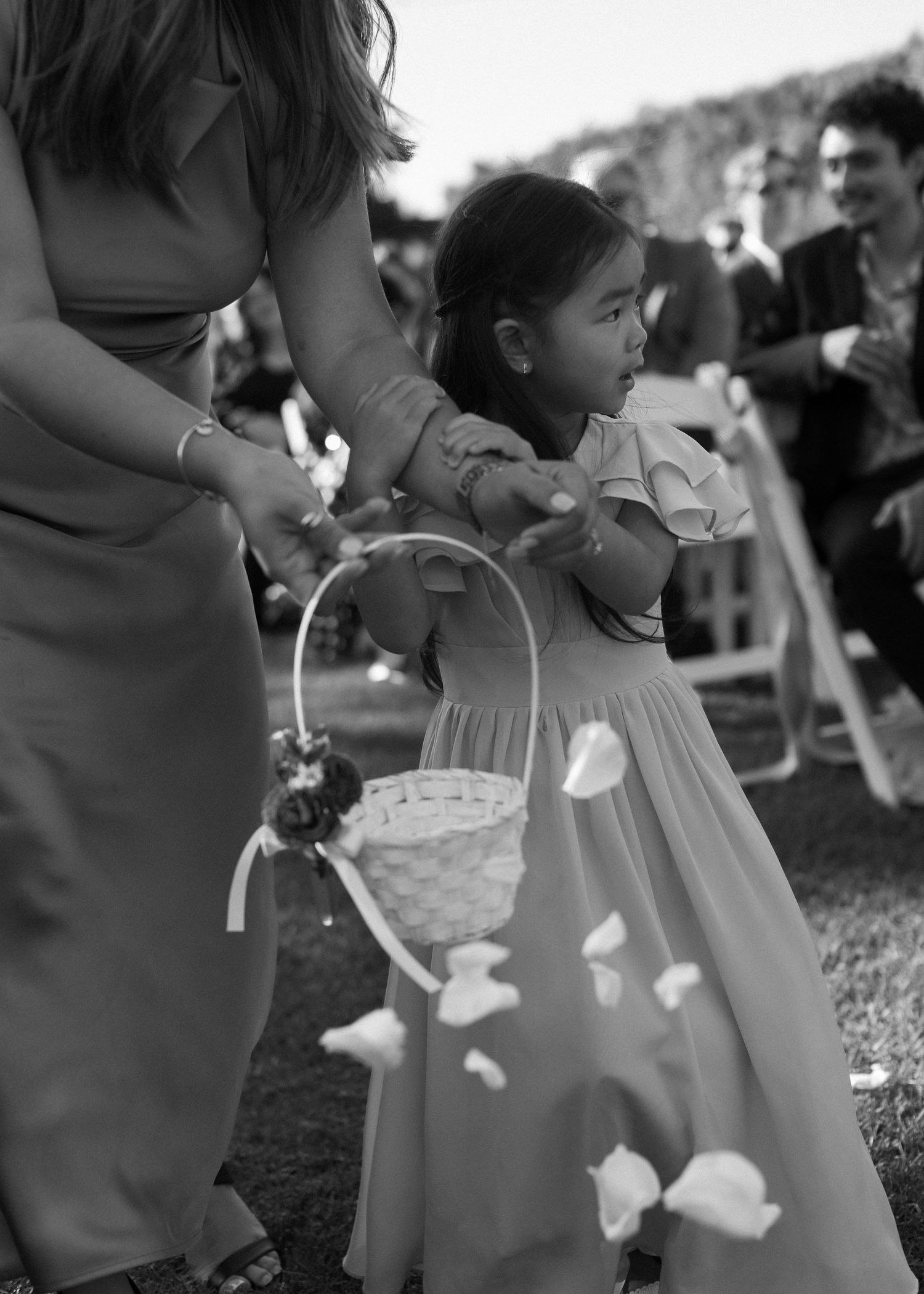Flower girls in white dresses carrying decorated baskets at outdoor wedding ceremony.