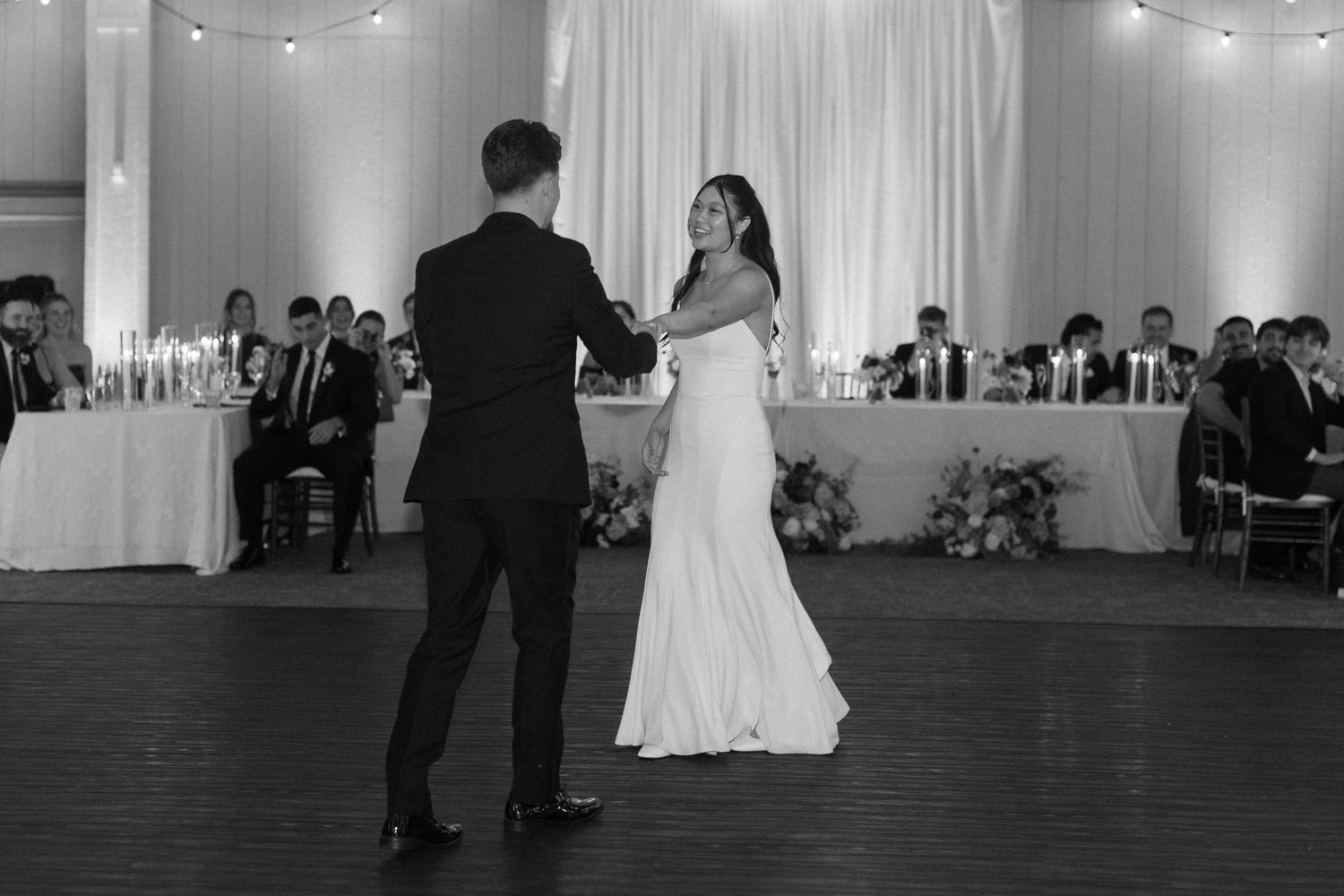 Black and white photo of first dance at wedding reception with string lights overhead.