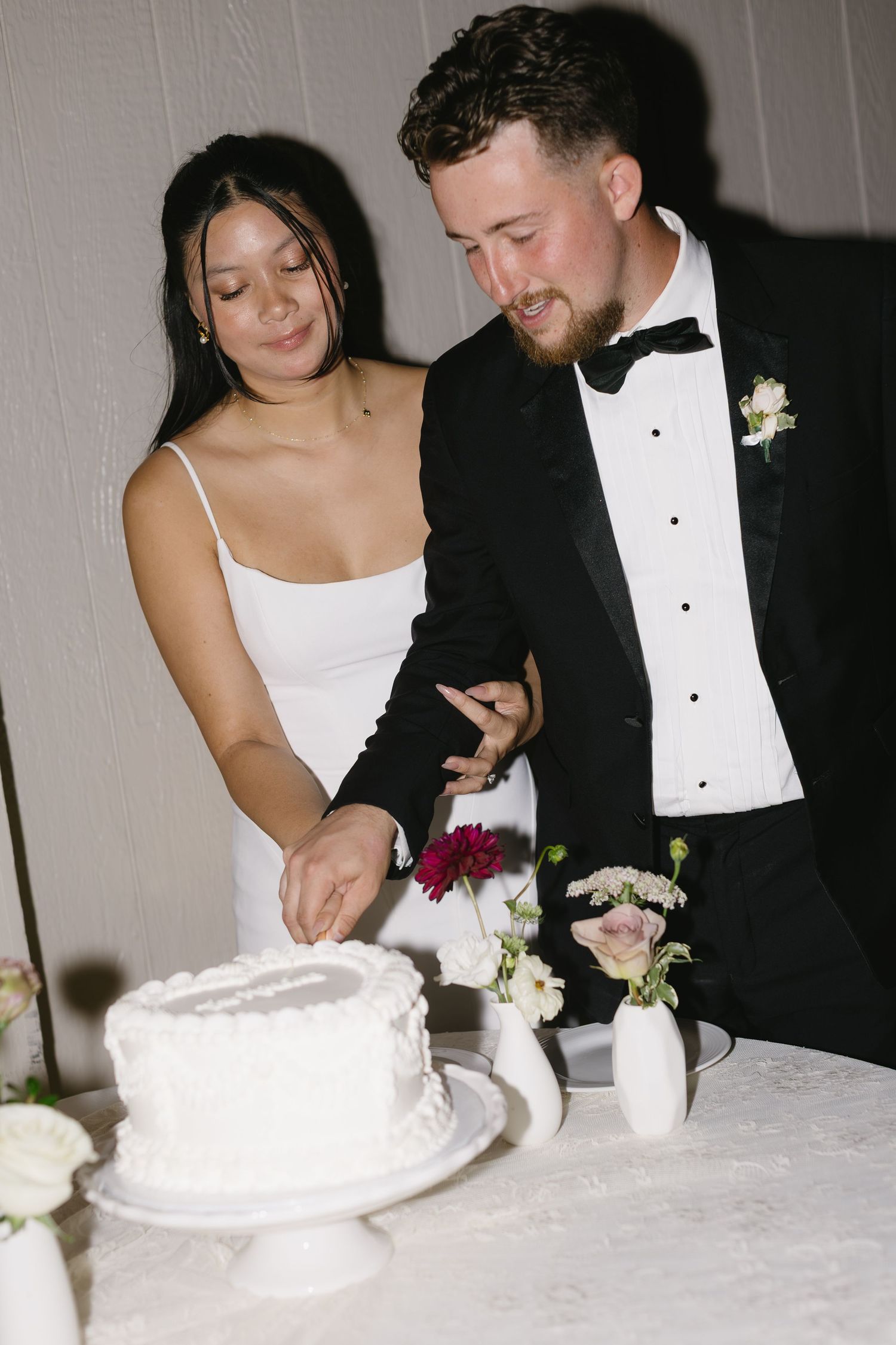 Newlyweds cutting their white wedding cake together at the reception.