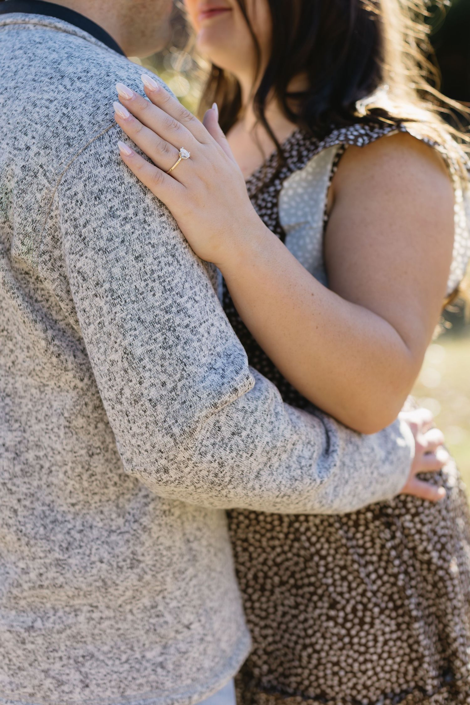 Close-up shot of an engagement ring as a couple embraces in casual outdoor wear.
