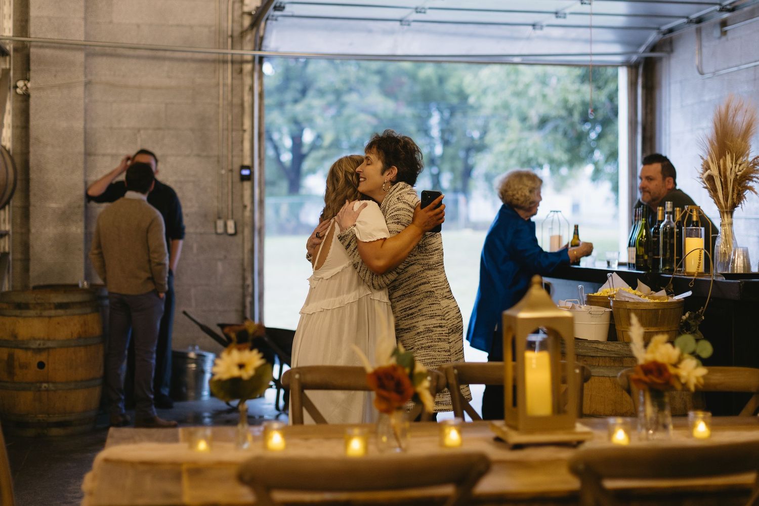 People gathering at a rustic venue with warm lighting and wine barrels in the background.