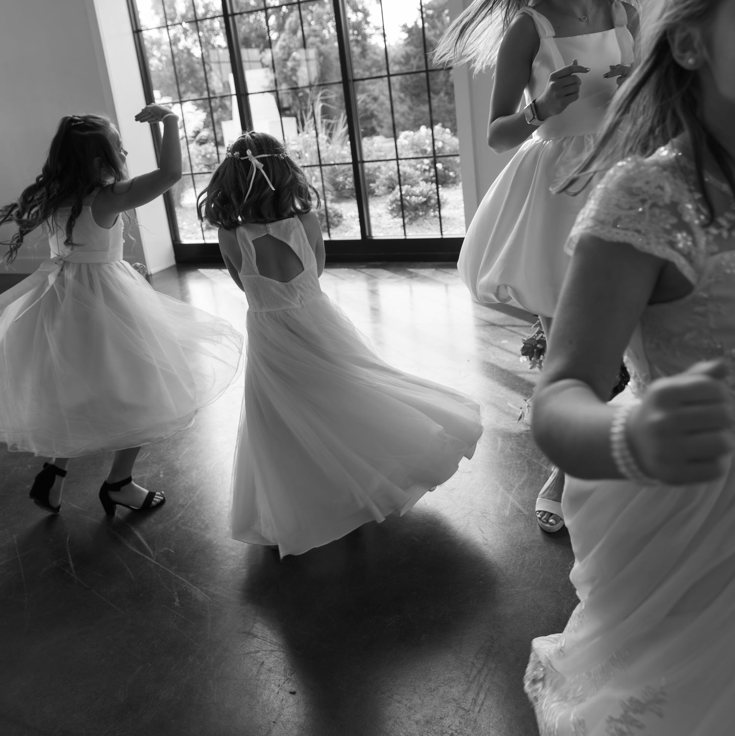 Black and white photo of people in white dresses twirling and dancing in a sunlit room.