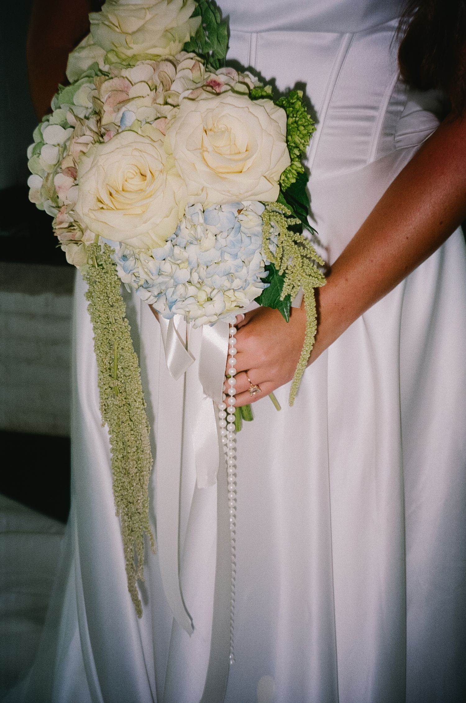 Bridal bouquet of white roses and hydrangeas with pearl details against white wedding dress.