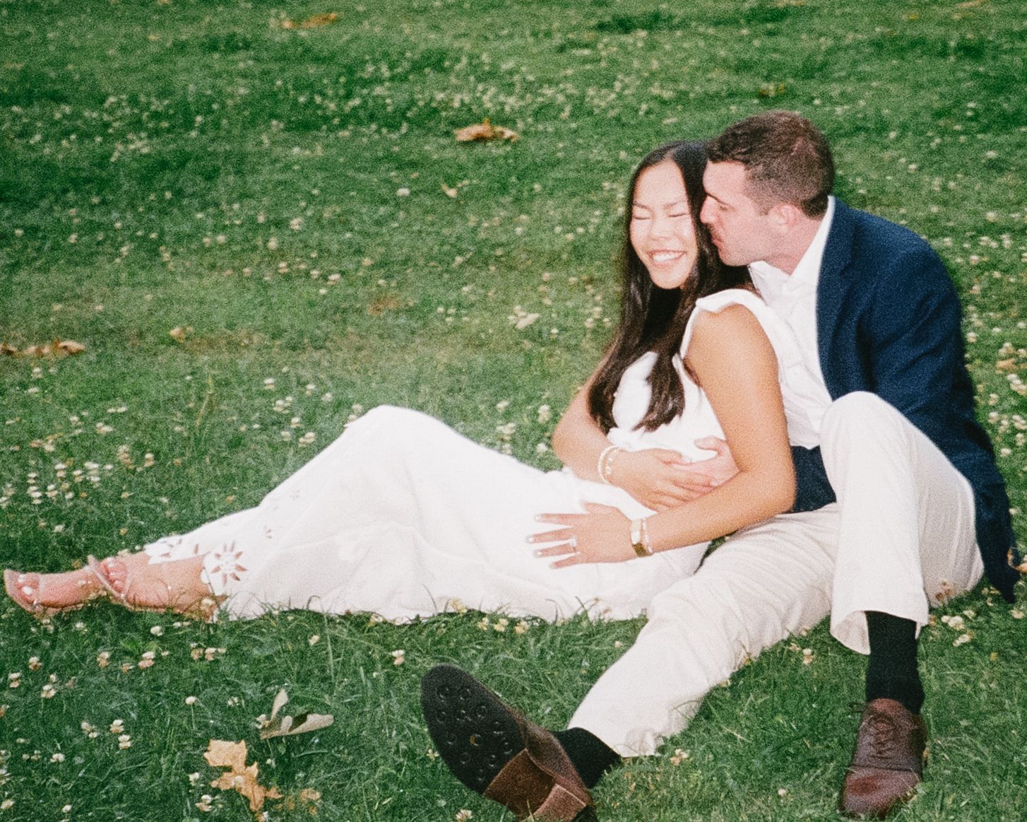 A couple in wedding attire relaxes together on a grassy lawn during a sunny day.