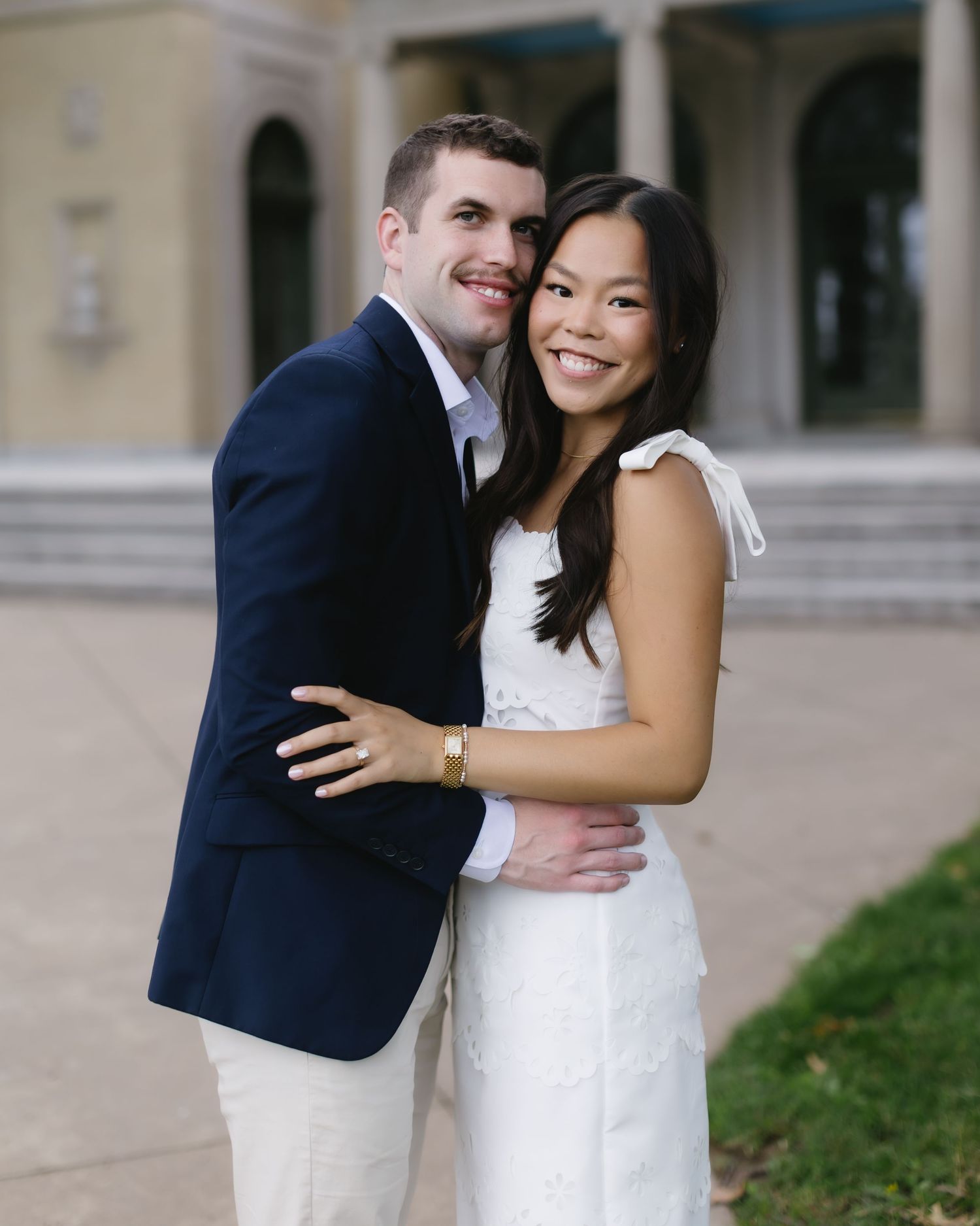 Happy couple embraces on stone portico of elegant building during photo session.