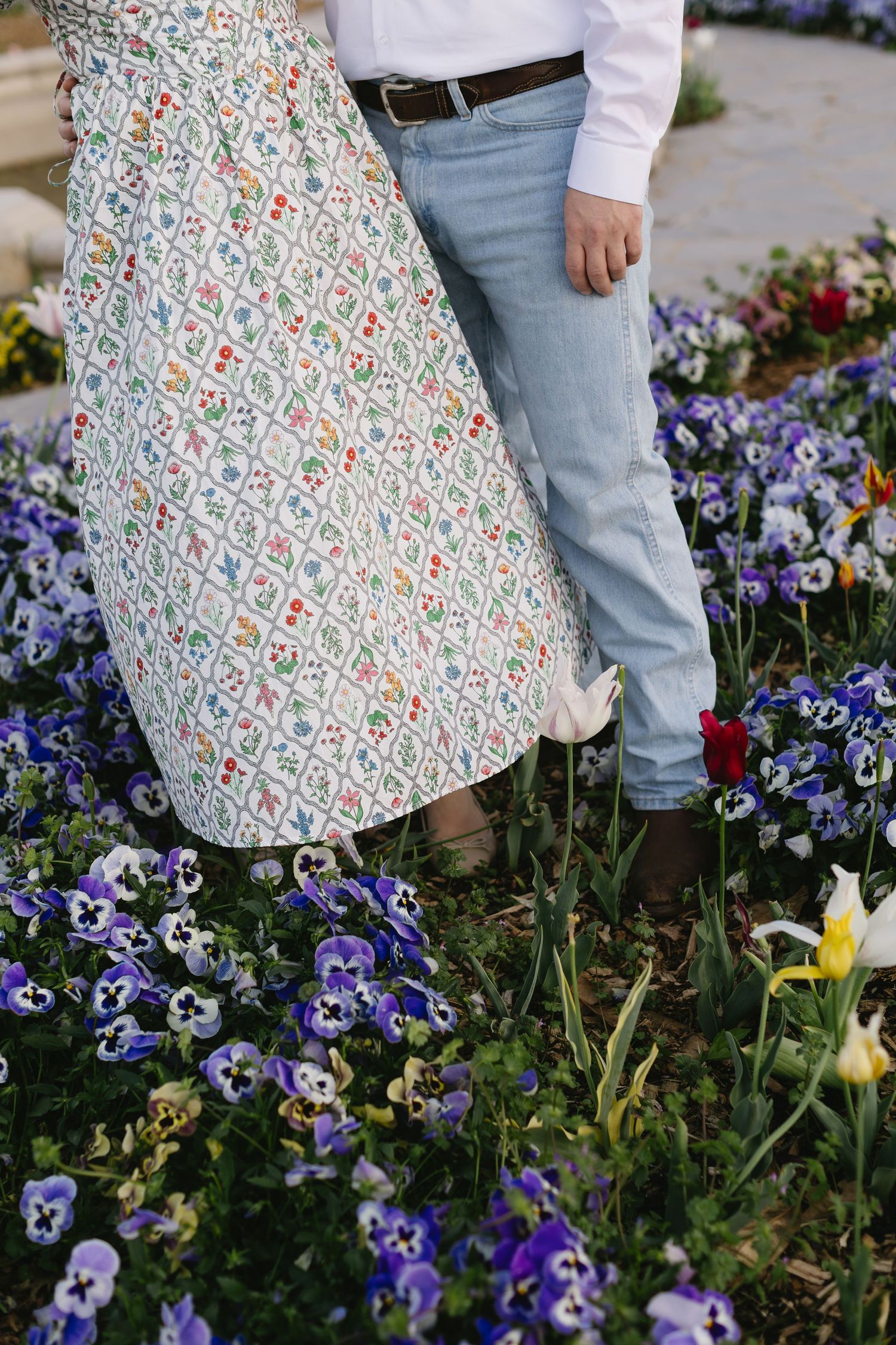 A floral print dress sways among purple pansies and yellow daffodils in a spring garden.