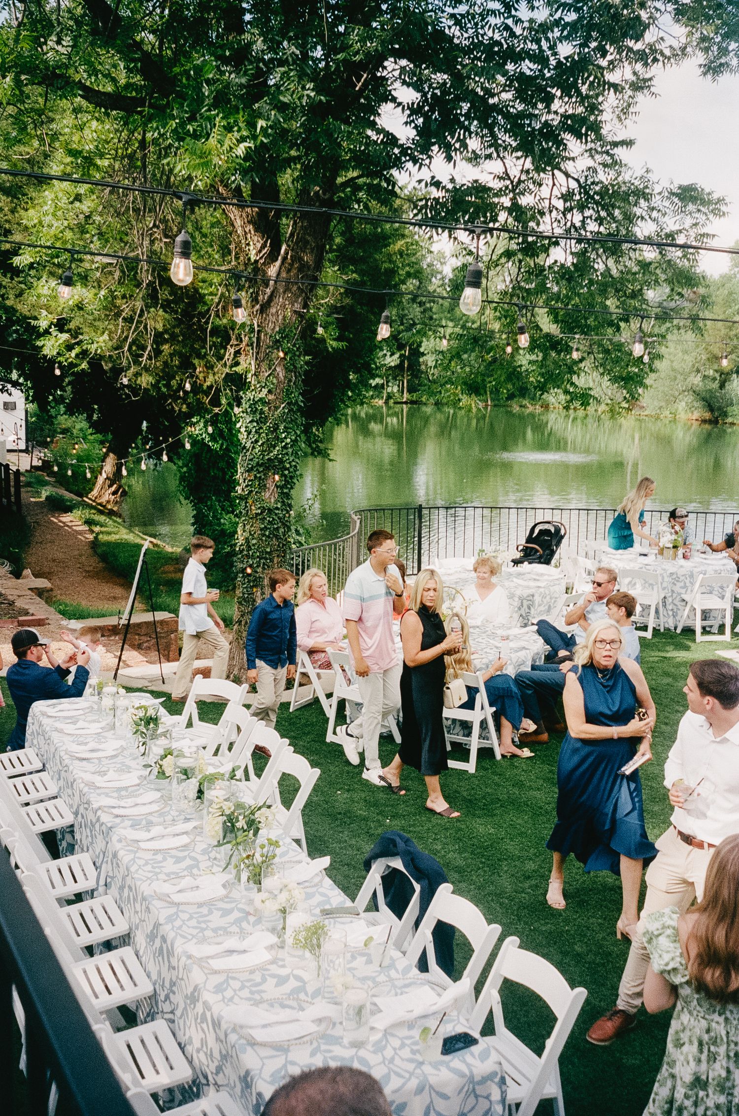 Outdoor wedding ceremony setup with white chairs and floral arrangements under leafy trees.